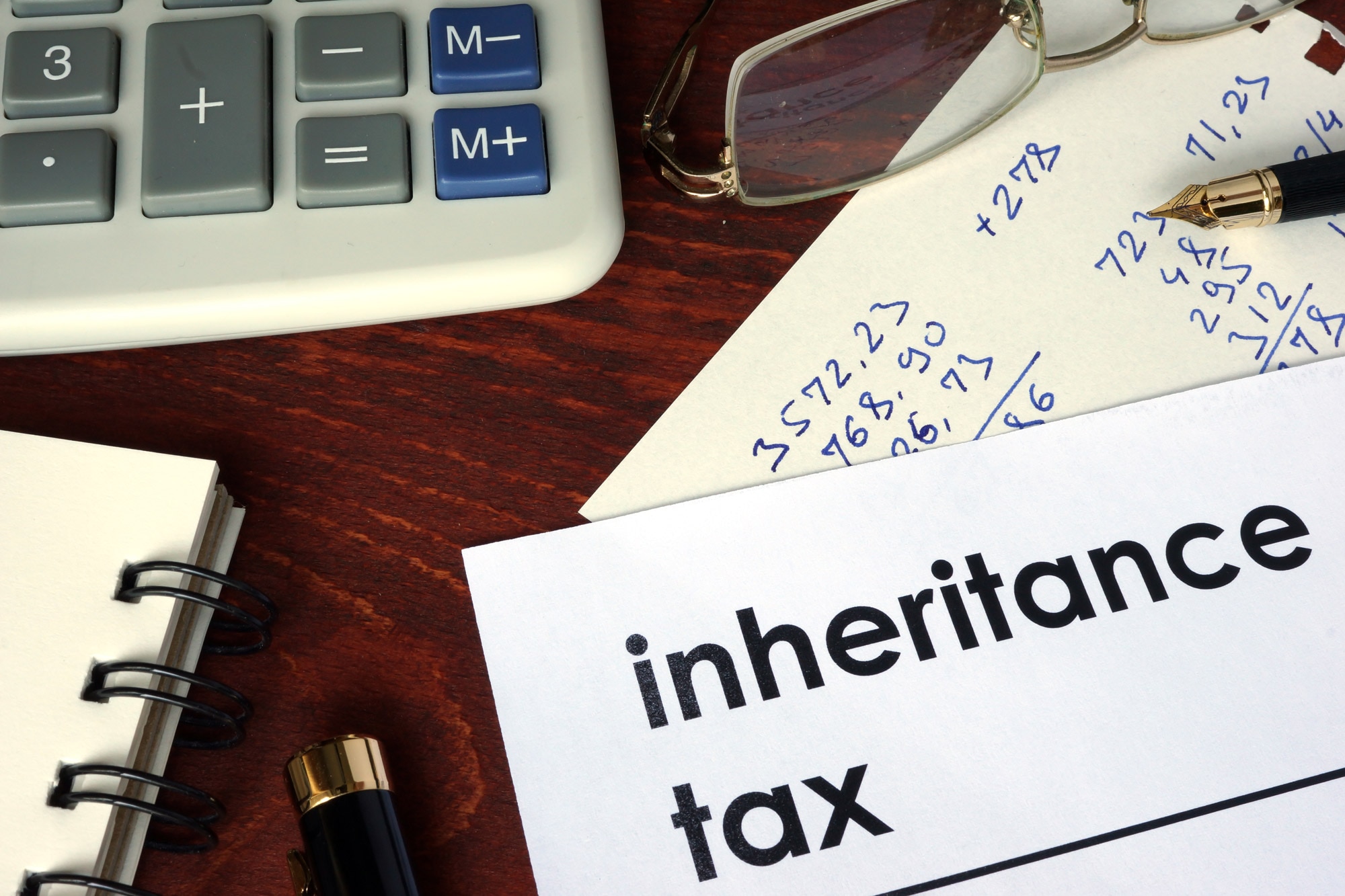 A table with glasses, pen, calculator and numbers depicting calculations for inheritance tax