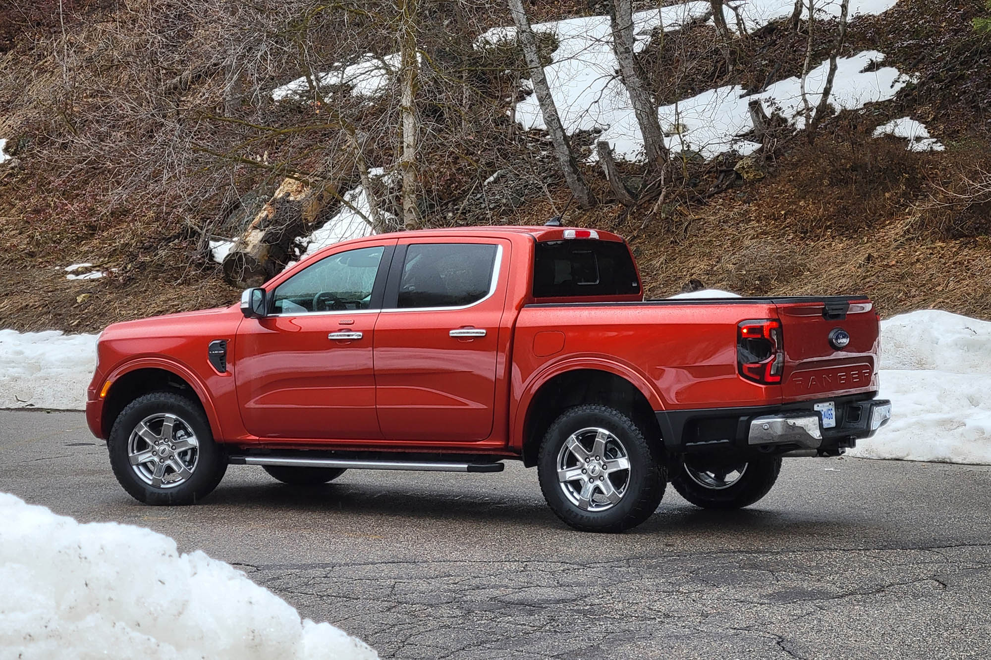 Red 2024 Ford Ranger Lariat on wet pavement by snowbanks.