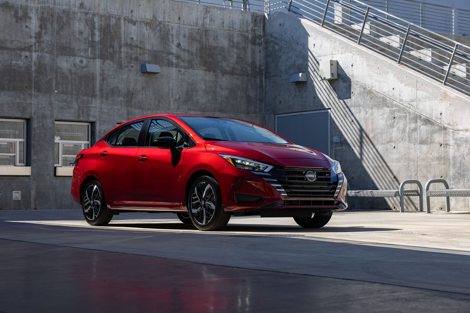 red Nissan Versa parked in an industrial area.