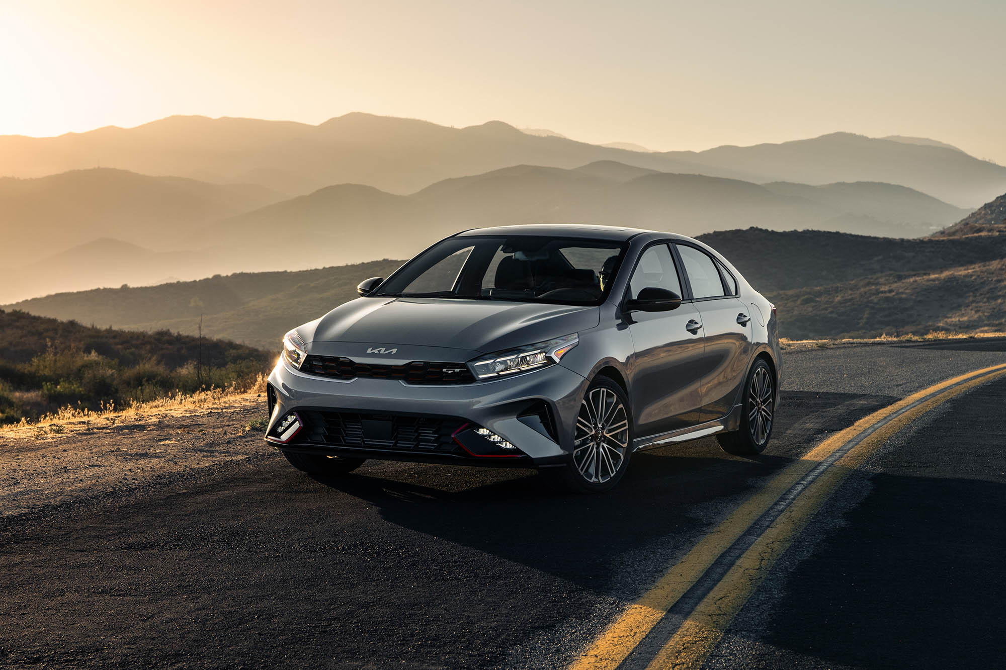 Kia Forte in silver parked on a road in front of mountains.