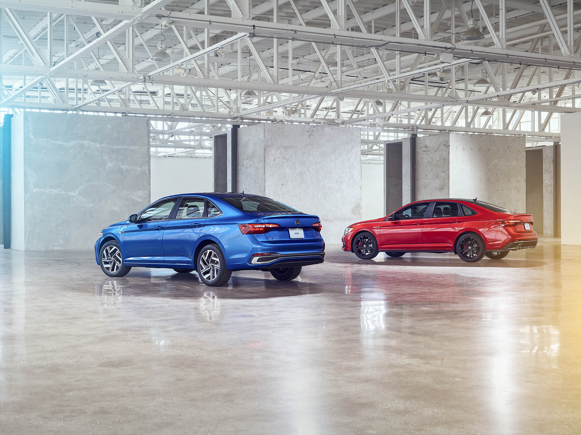 Two Volkswagen Jettas in blue and red parked in a warehouse.