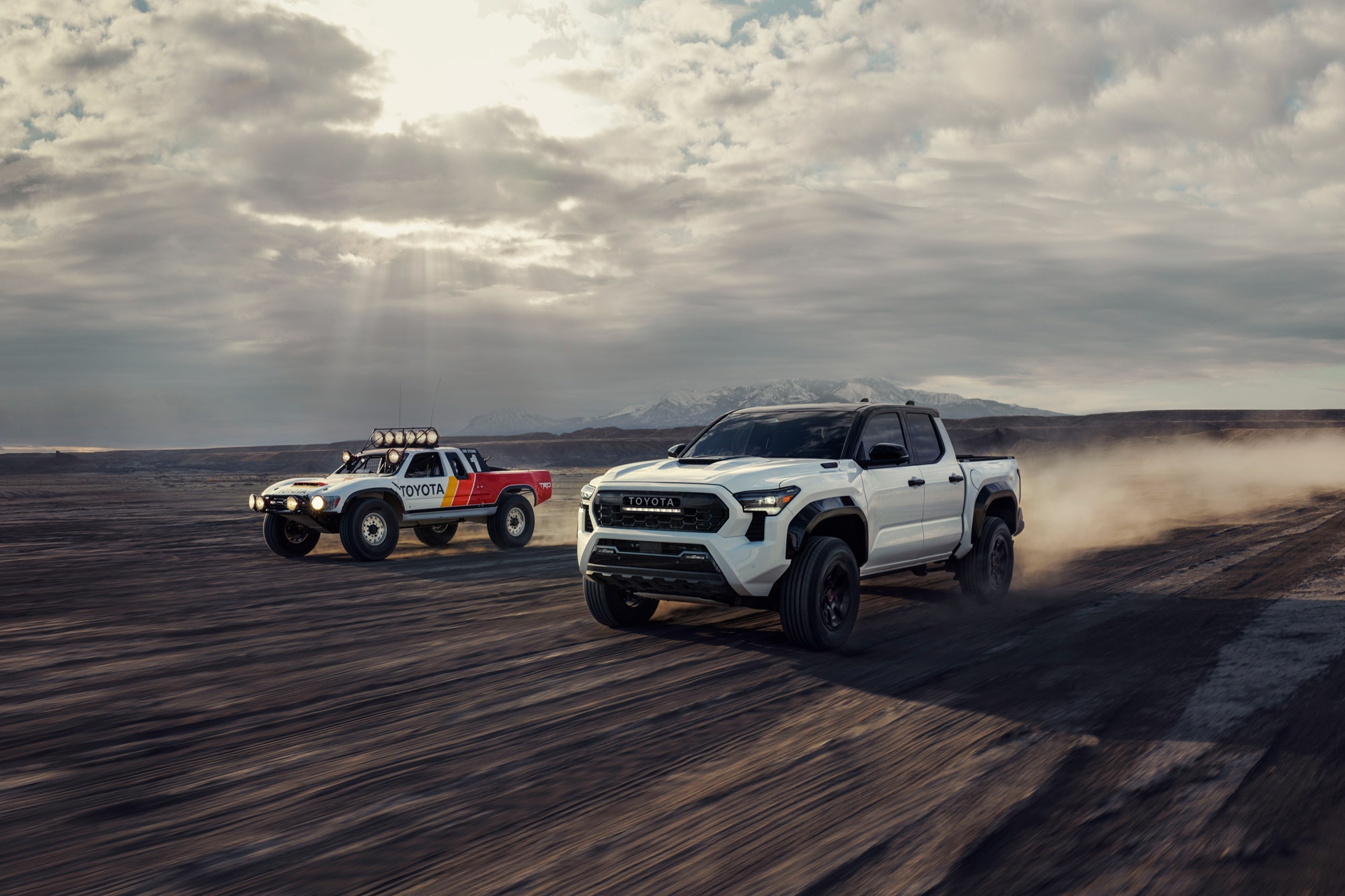 2024 Toyota Tacoma TRD Pro drives next to vintage Toyota race truck.