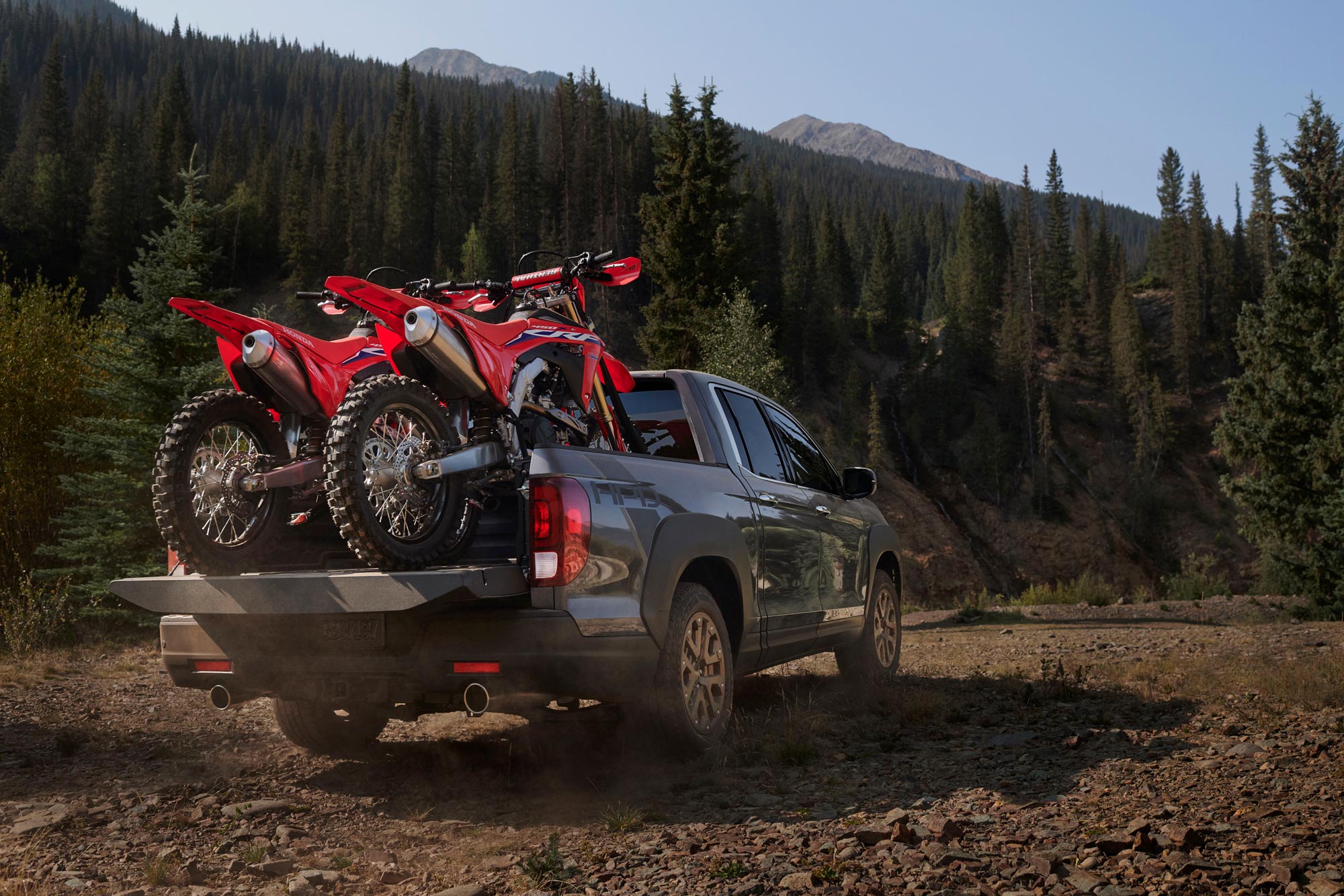 Honda Ridgeline driving off-road with two motorcycles in bed.
