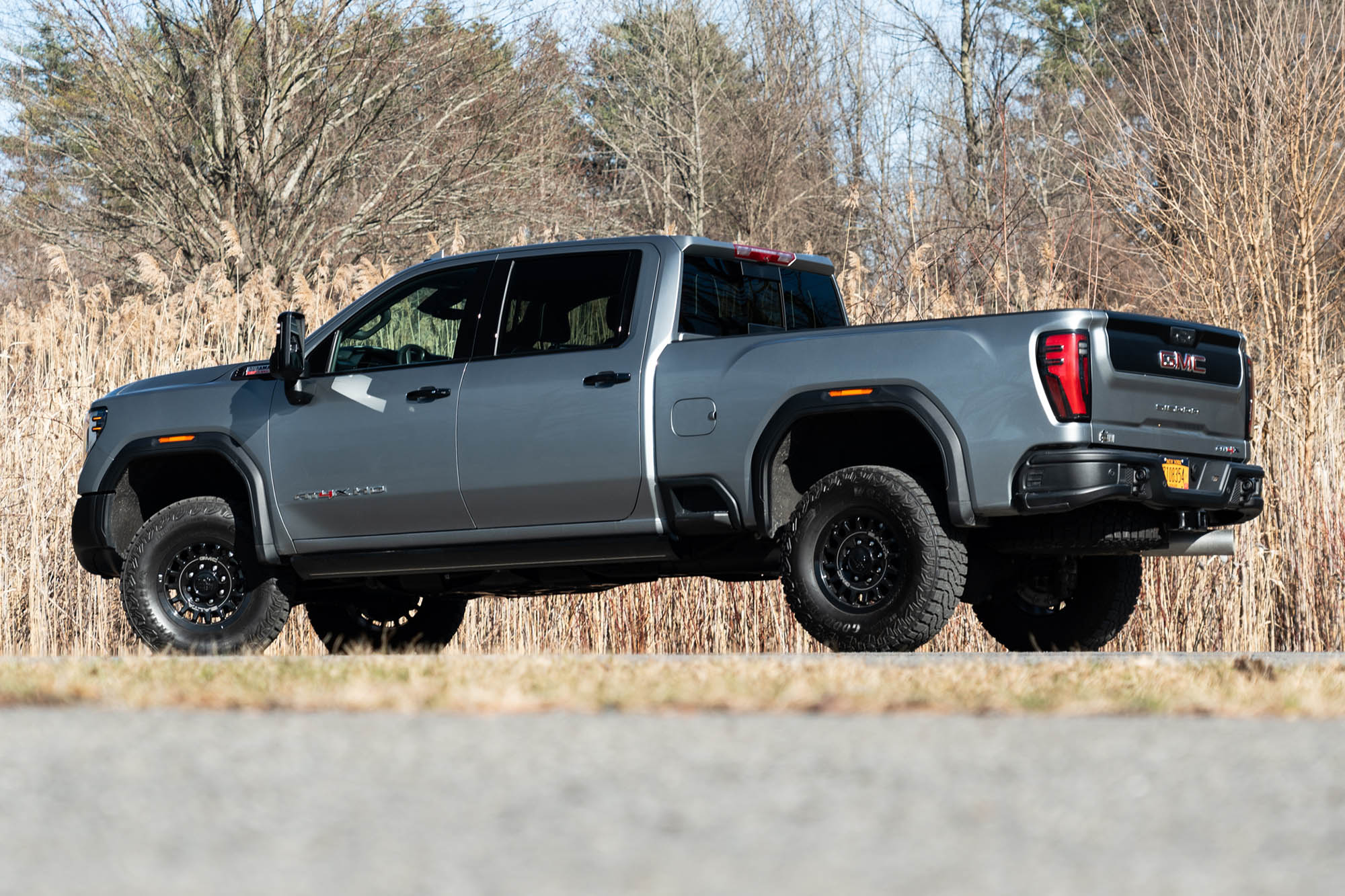 Rear view of a gray 2024 GMC Sierra 2500HD with the AT4X AEV package parked on pavement near some trees.