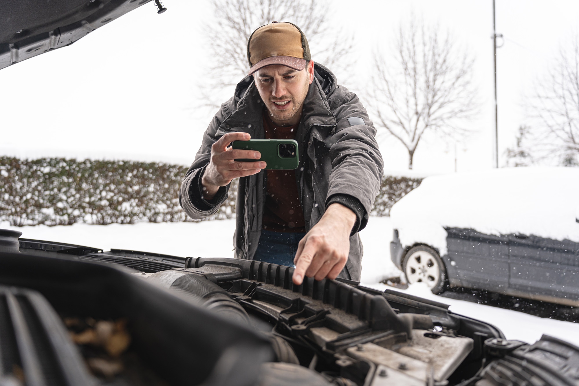 Man pointing at engine bay while taking video with his phone in the snow