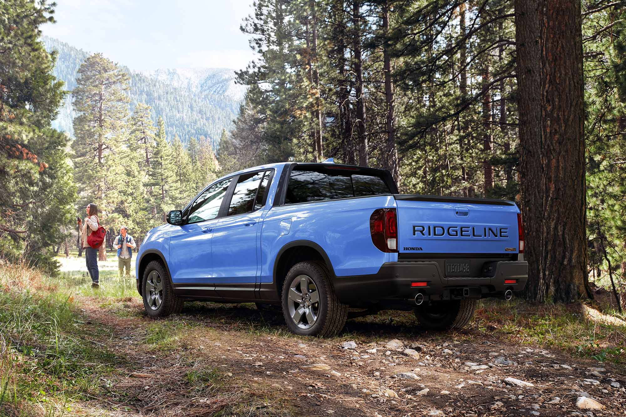 Blue Honda Ridgeline parked in forest with hikers standing nearby.