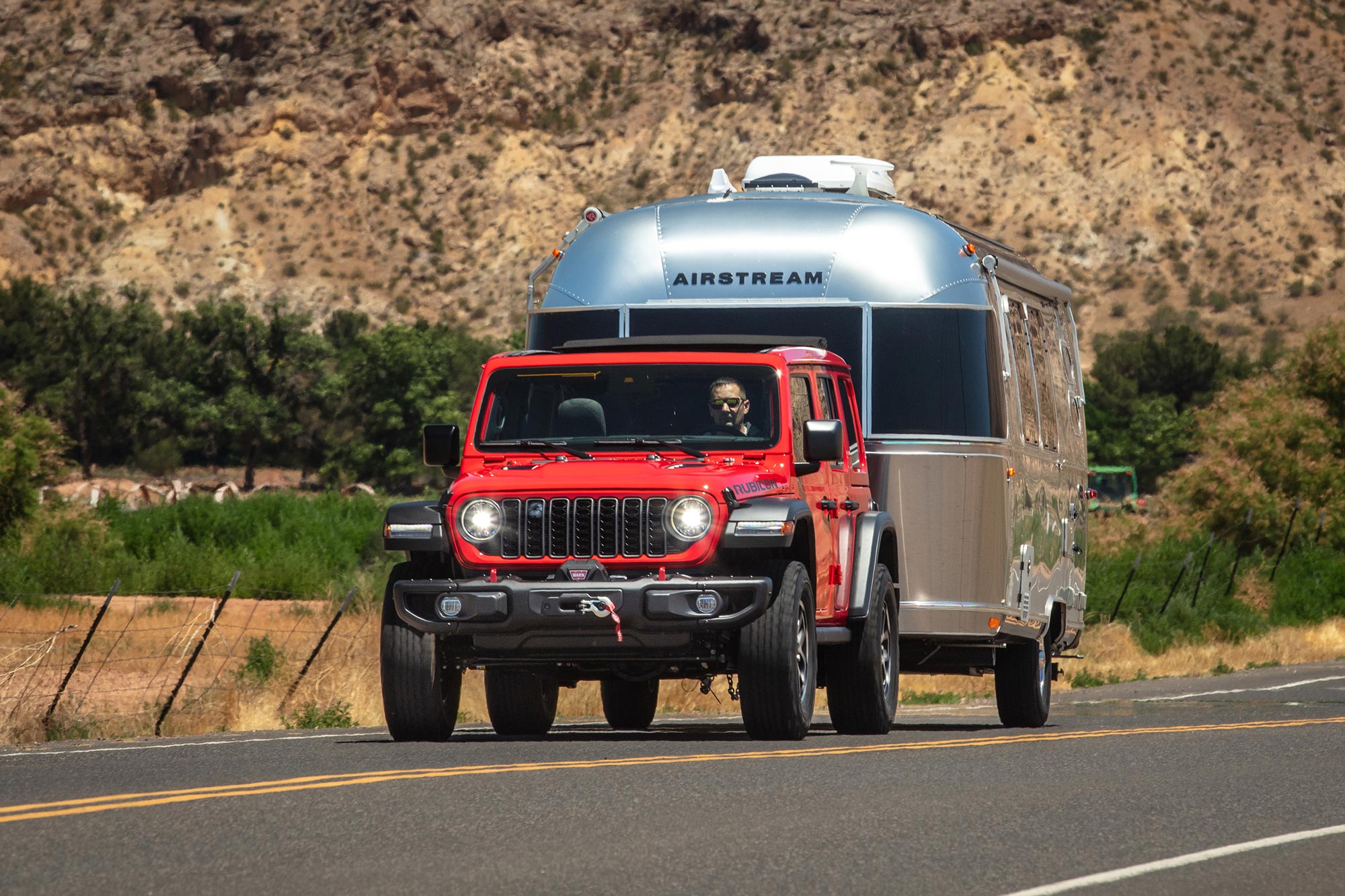 A red Jeep Wrangler Rubicon towing a silver Airstream trailer