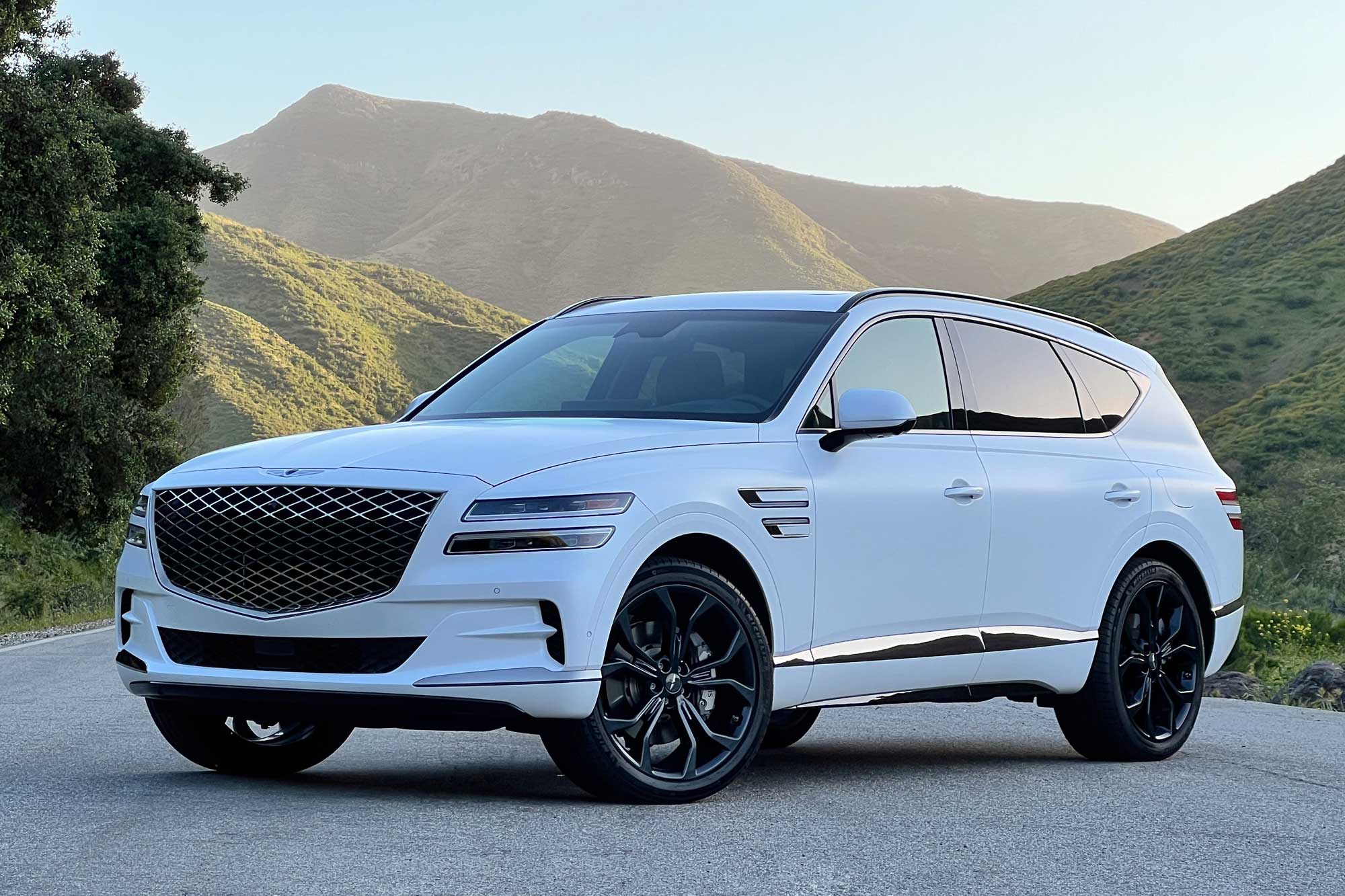 Front-quarter view of a white 2024 Genesis GV80 3.5T Prestige Signature with sunlit mountains in the background.