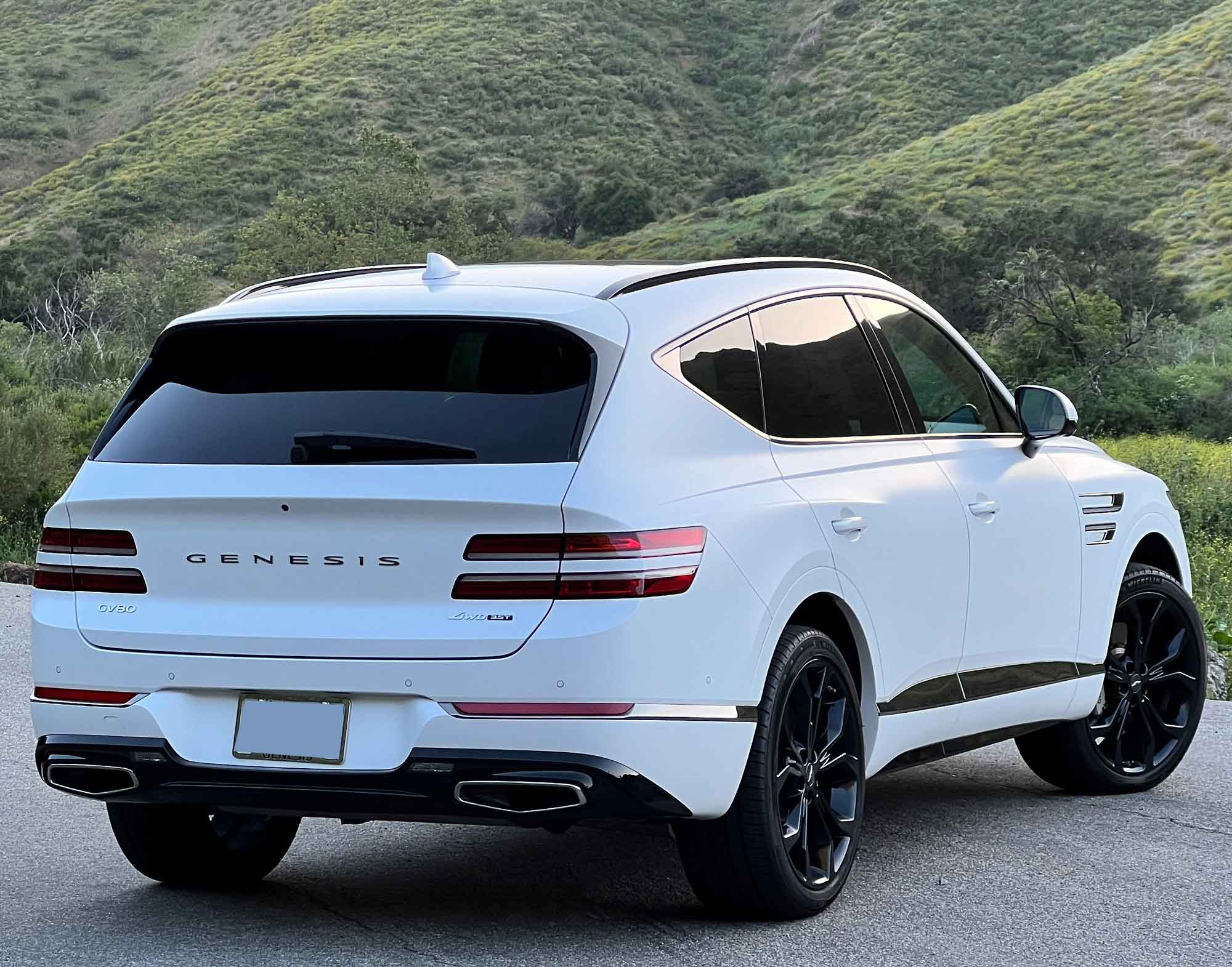 Rear-quarter view of a white 2024 Genesis GV80 3.5T Prestige Signature with mountains in the background.