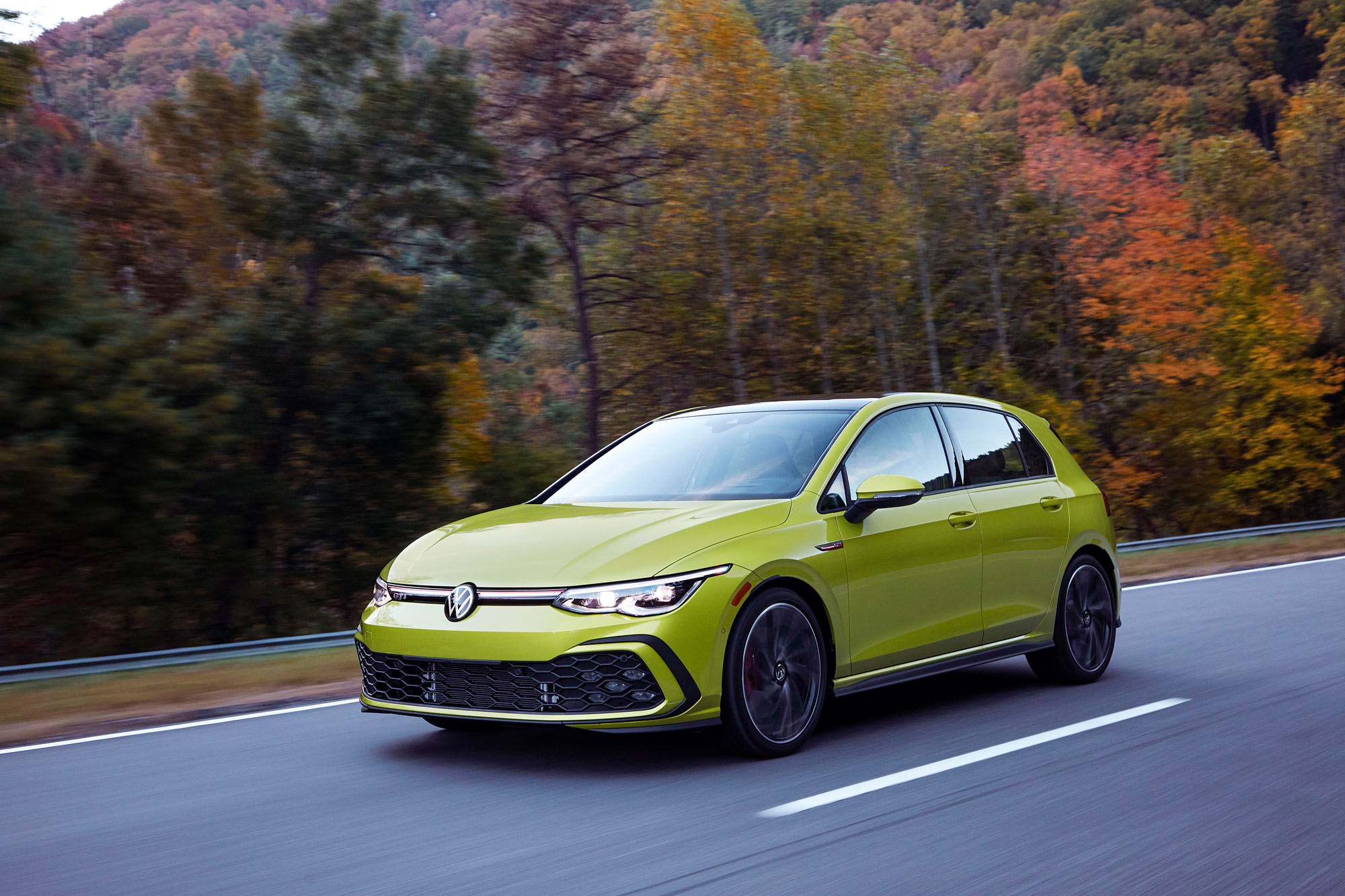 Green Volkswagen GTI driving on a highway.