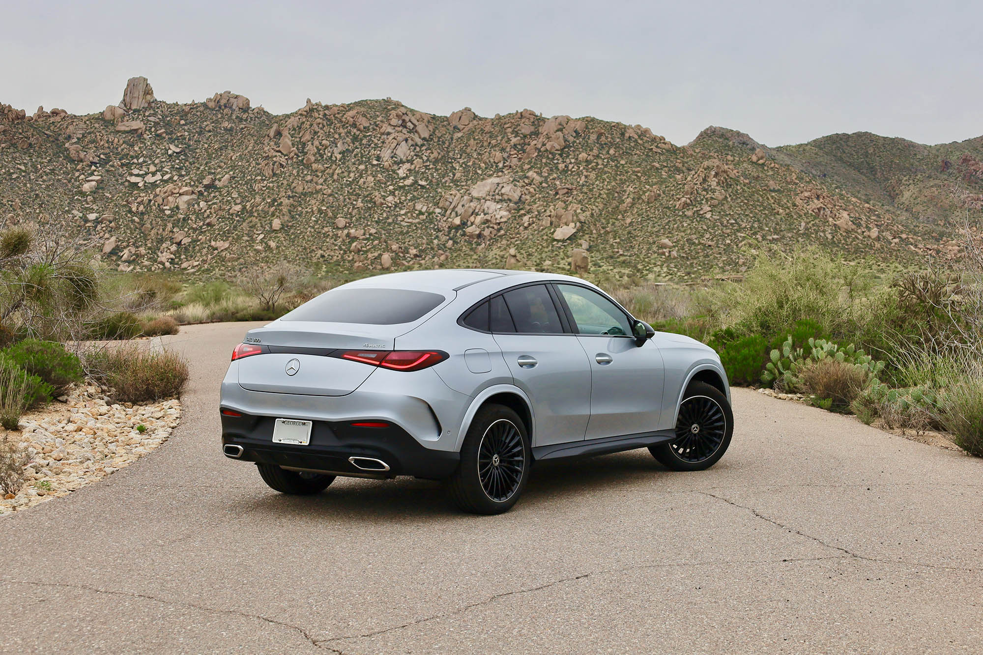 Rear-quarter view of a silver 2024 Mercedes-Benz GLC 300 parked on the pavement in the Arizona desert with mountains in the background.