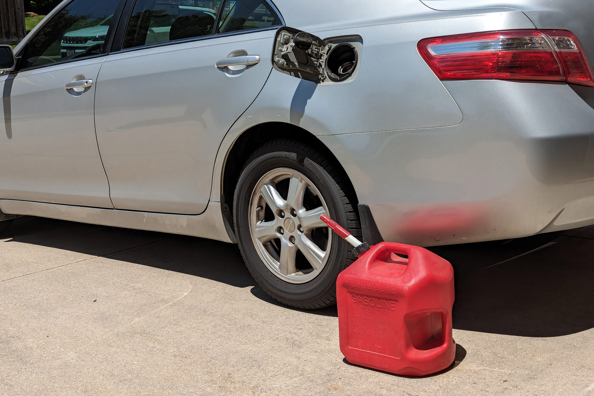 Red gas container sits next to a silver car with its fuel door open.