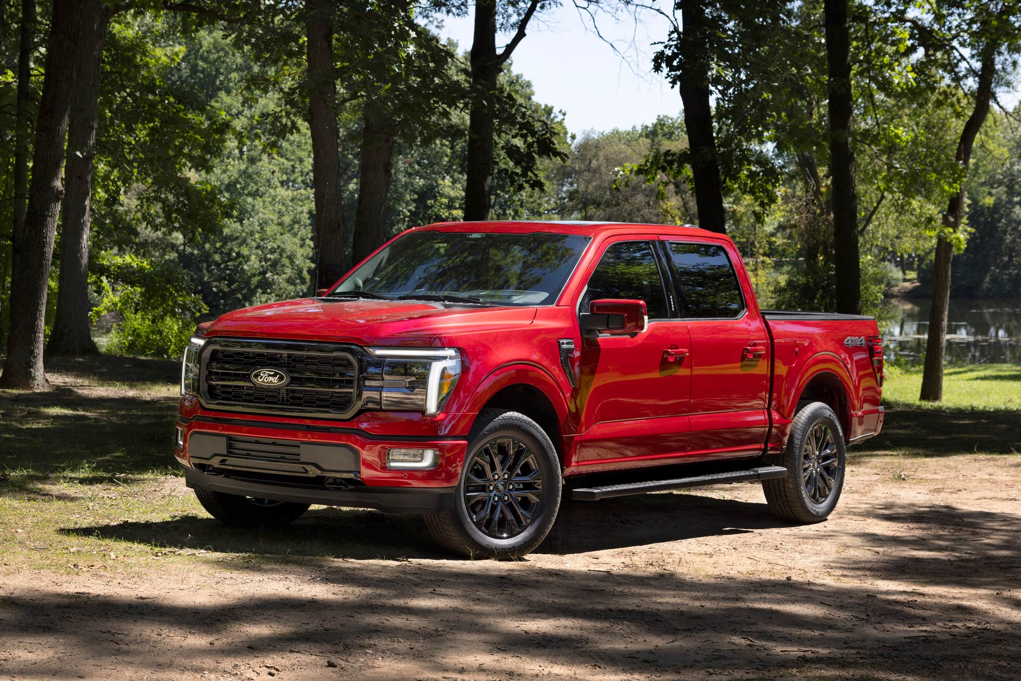 Red 2024 Ford F-150 Lariat parked under trees on dirt.