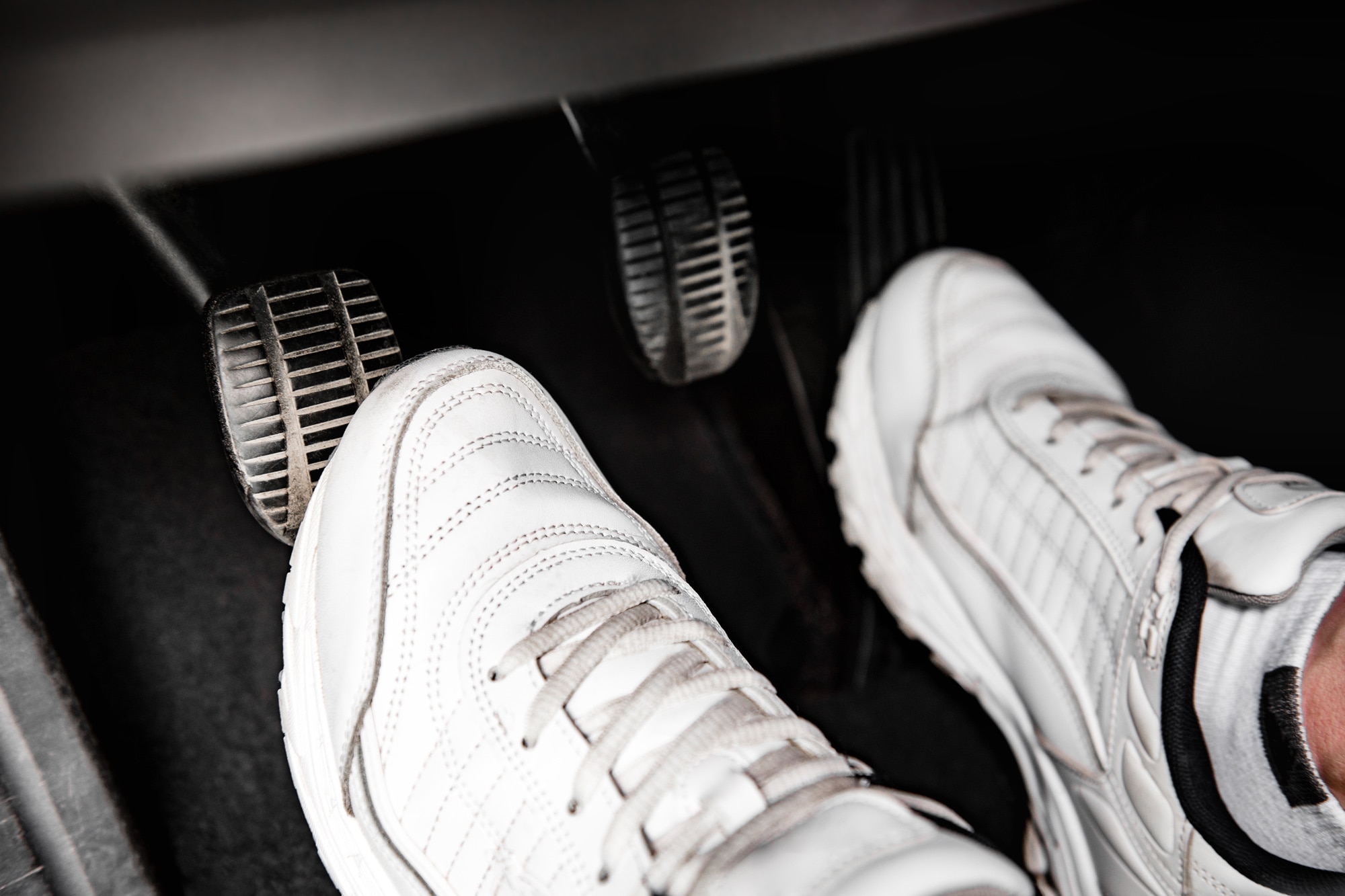 Close-up of a person with white shoes pressing the clutch pedal of a car.