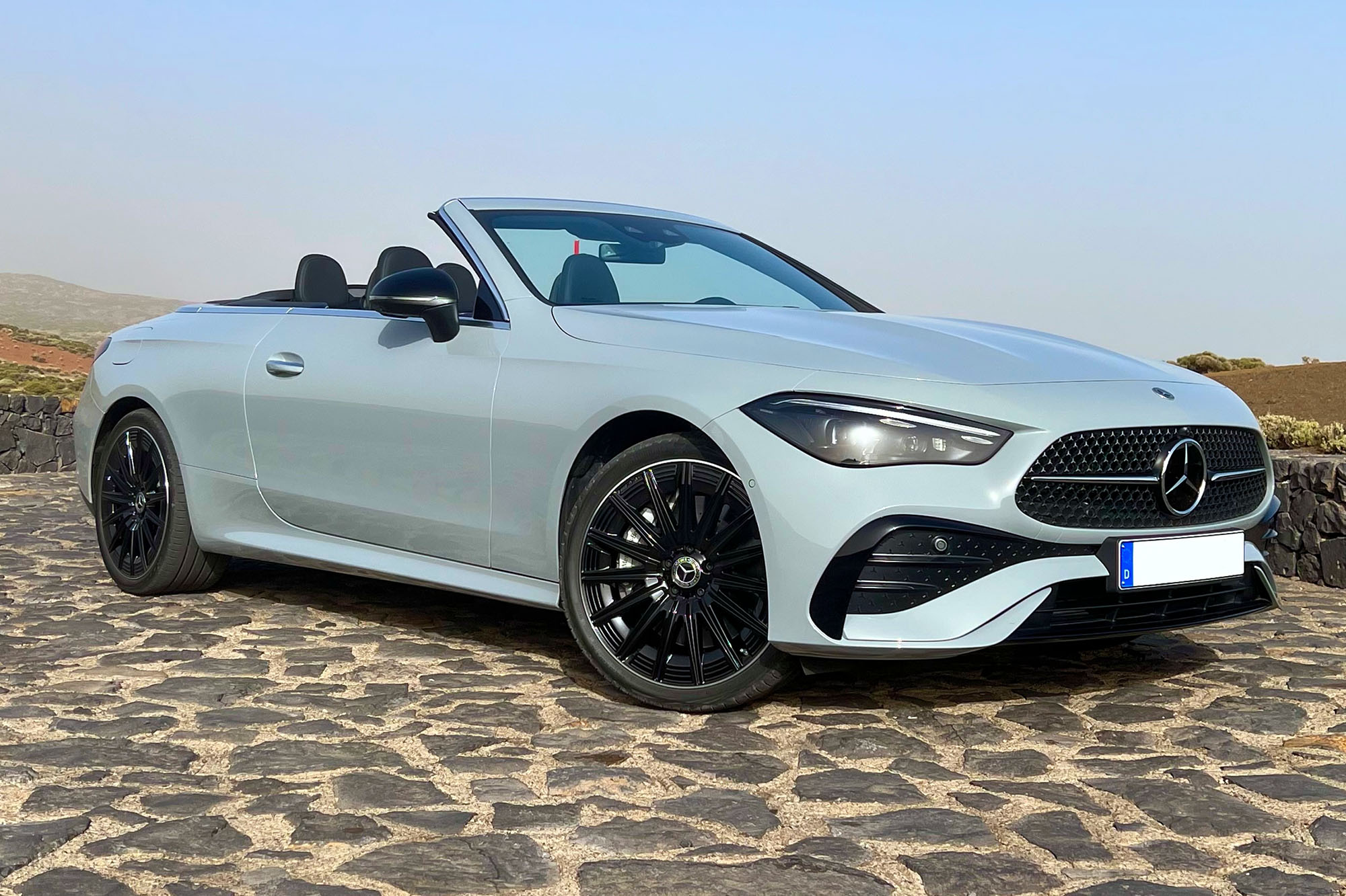 Front-quarter view of a 2024 Mercedes-Benz CLE 450 Cabriolet, parked with the top down on a sunny day on a cobblestone surface.