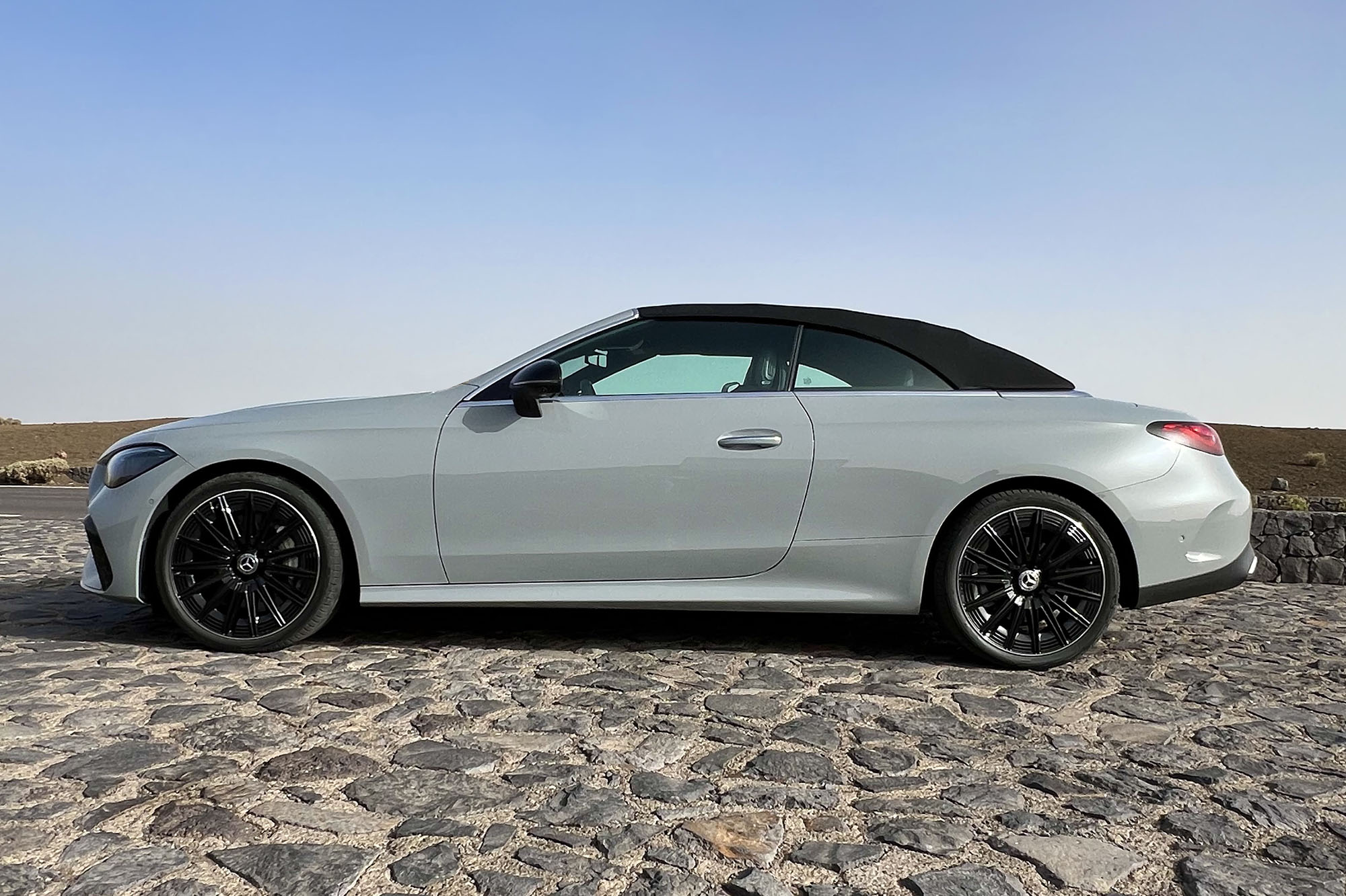 Side view of a 2024 Mercedes-Benz CLE 450 Cabriolet, parked with the top up on a sunny day on a cobblestone surface.