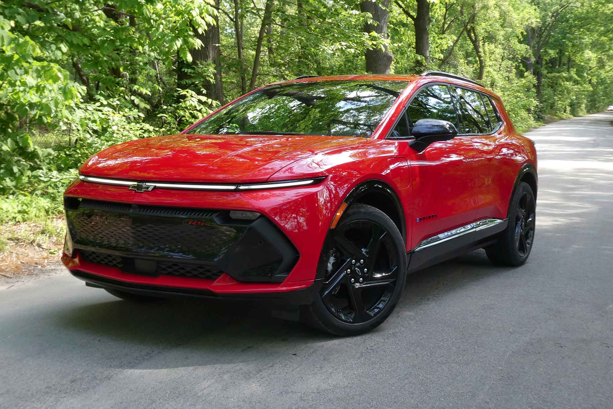 Front-quarter view of a red 2024 Chevrolet Equinox EV 3RS parked on a tree-lined road