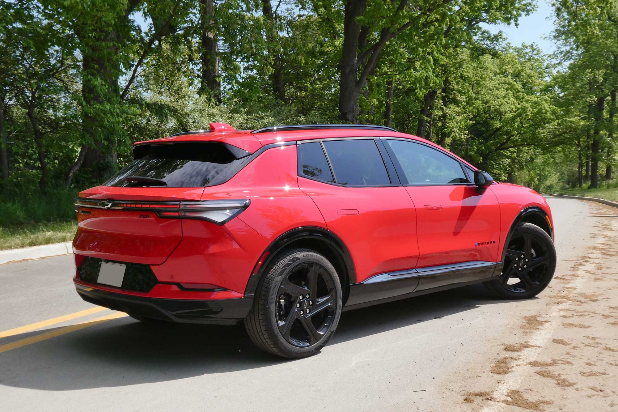 Rear-quarter view of a red 2024 Chevrolet Equinox EV 3RS parked on a tree-lined road