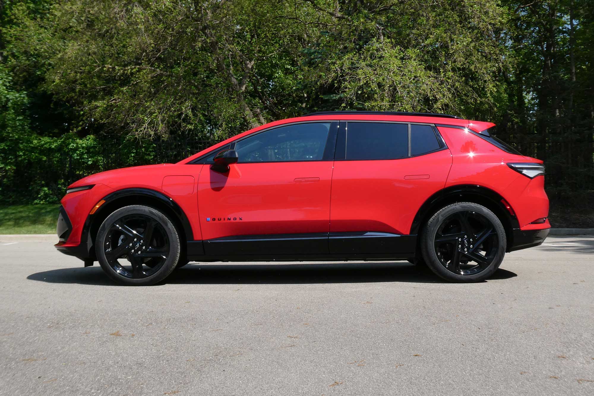 Side-quarter view of a red 2024 Chevrolet Equinox EV 3RS parked on the pavement with trees in the background