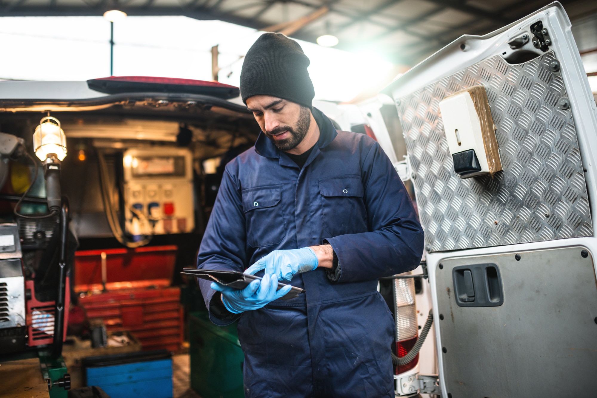 Mobile mechanic in blue overalls working on tablet next to his open van
