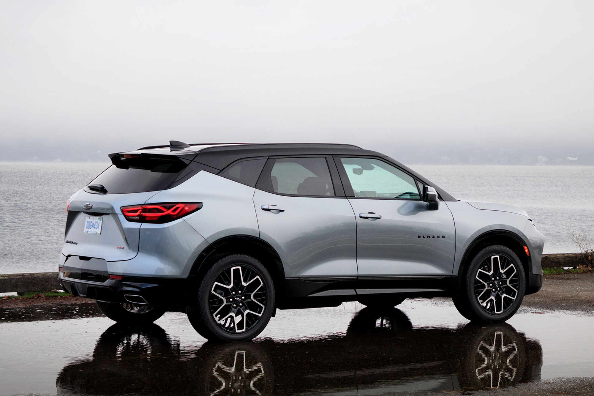 Rear quarter view of a silver 2024 Chevrolet Blazer RS parked in a puddle with the ocean in the background.