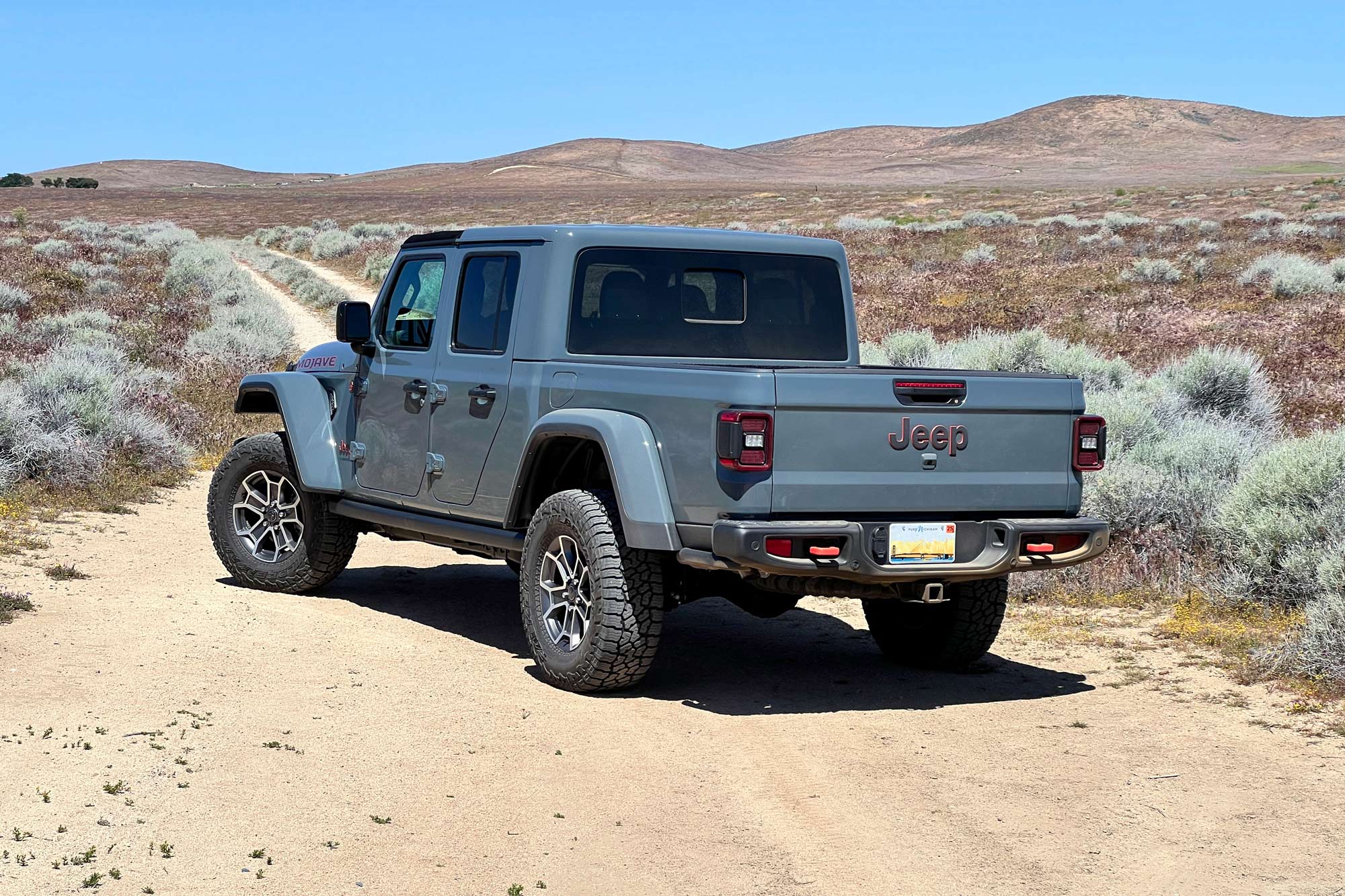 Rear-quarter of a 2024 Jeep Gladiator Mojave X with Anvil paint parked on a high desert trail