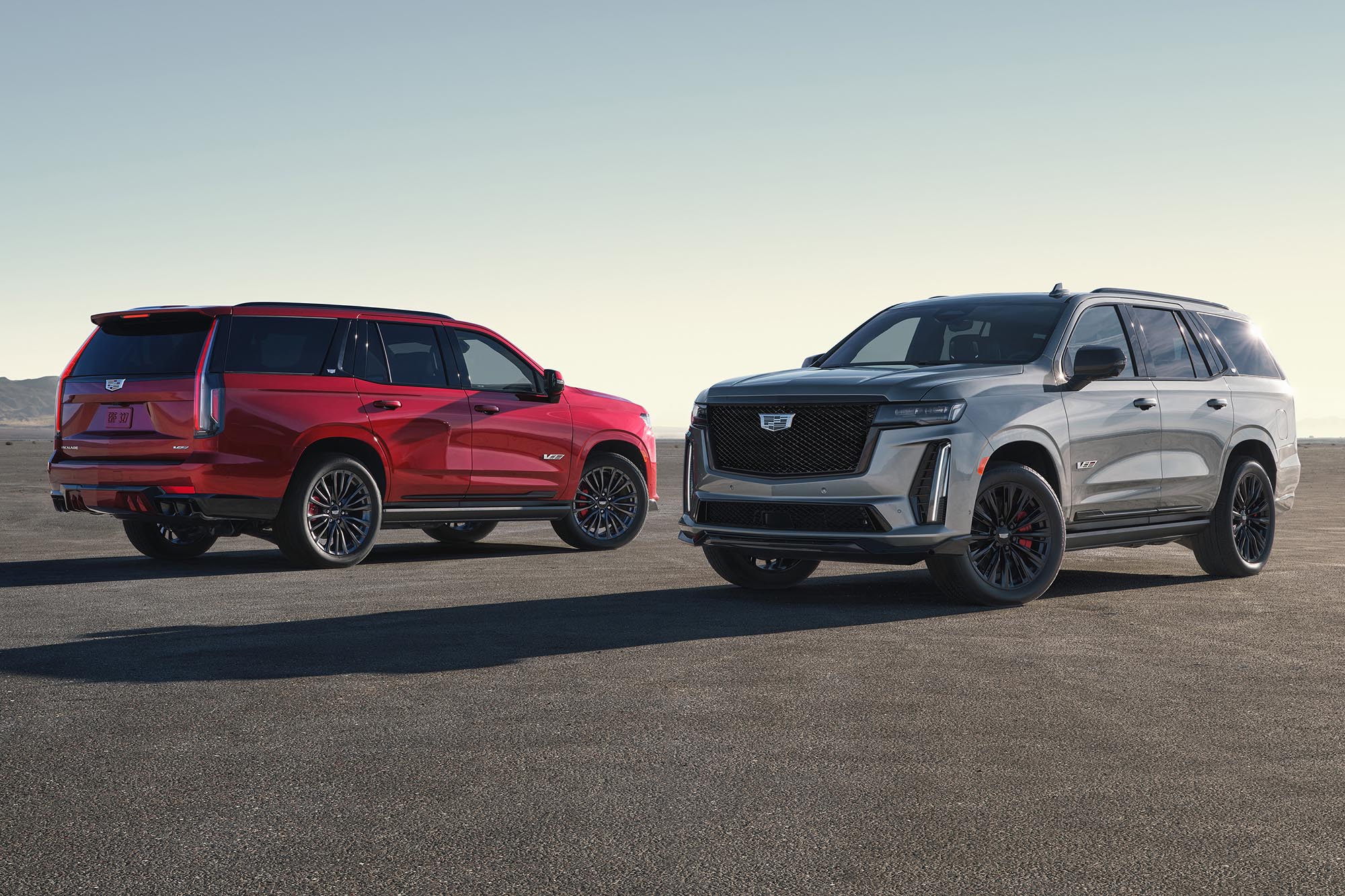 A red Cadillac Escalade and a gray Cadillac Escalade parked next to each other