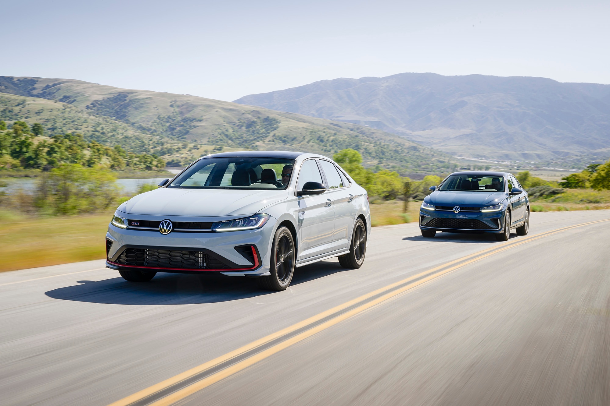 Light gray 2025 Volkswagen Jetta GLI driving in front of a blue 2025 VW Jetta