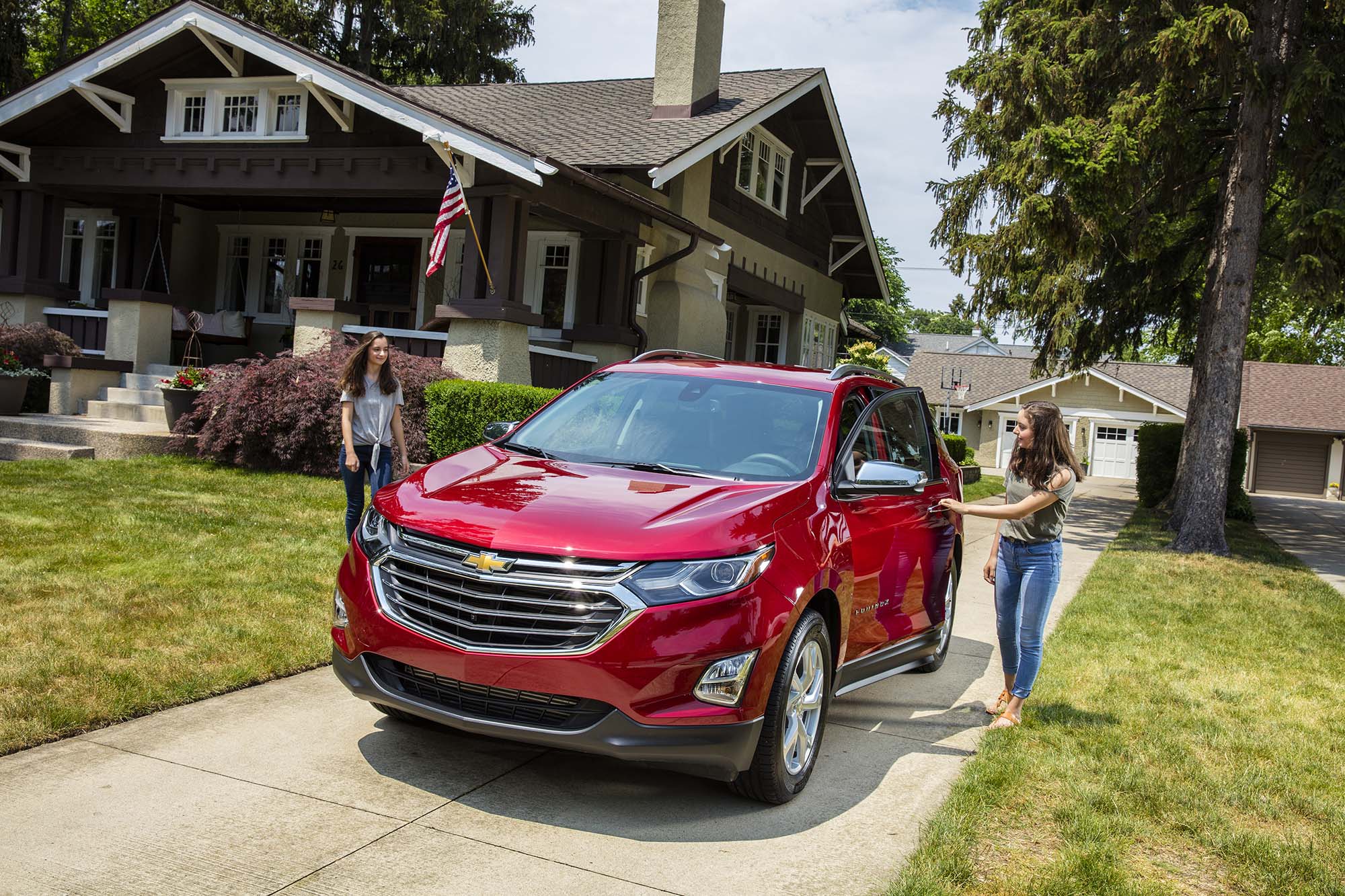 Two teenage people next to the front doors of a red Chevrolet Trailblazer.