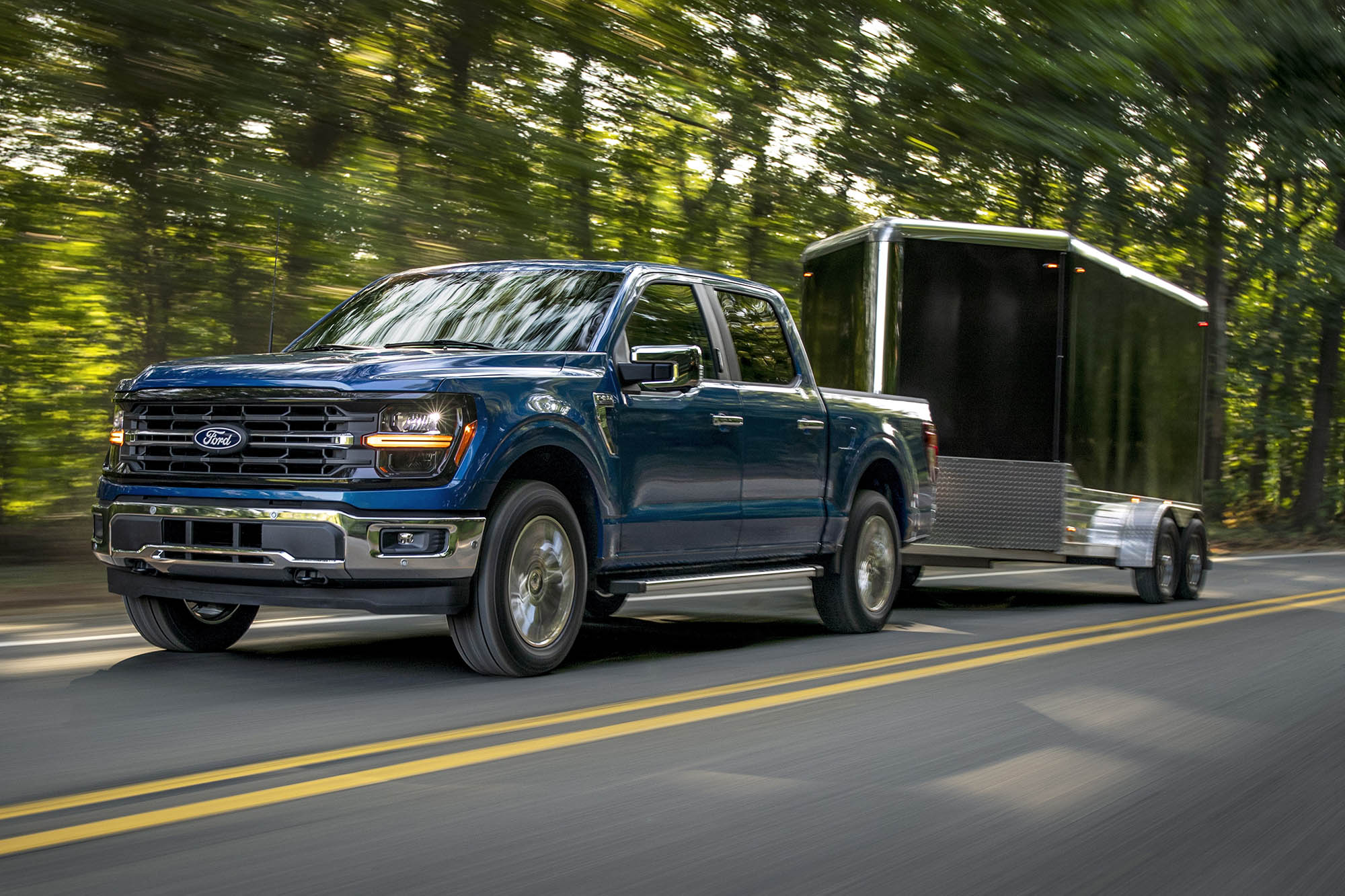 Ford F-150 in blue towing an enclosed trailer on a paved road.