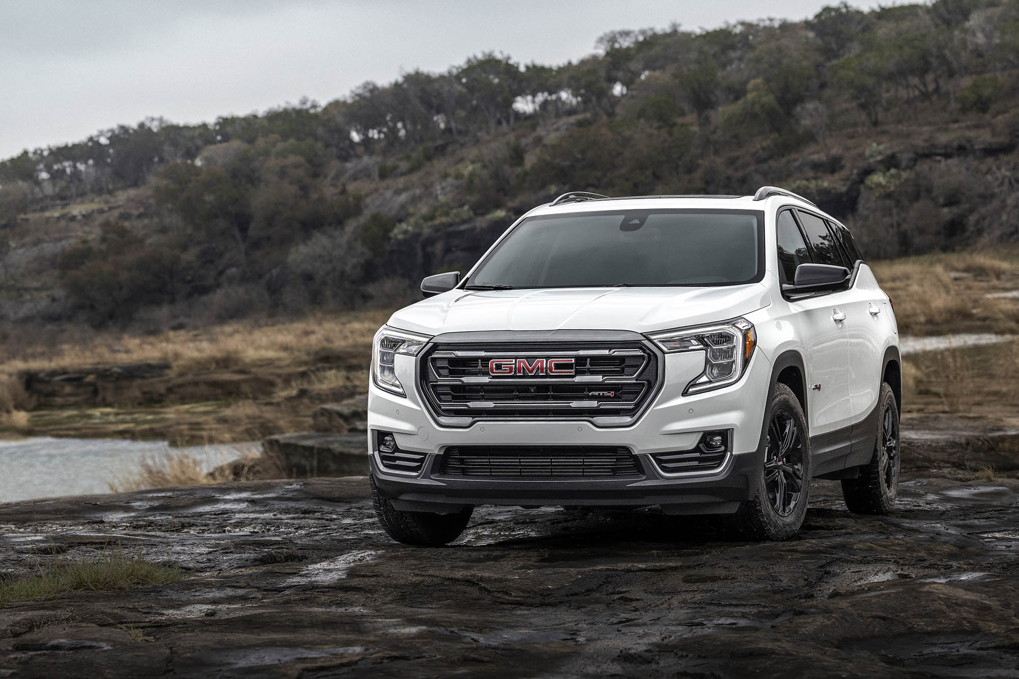 GMC Terrain in white parked on rocky land next to a body of water.