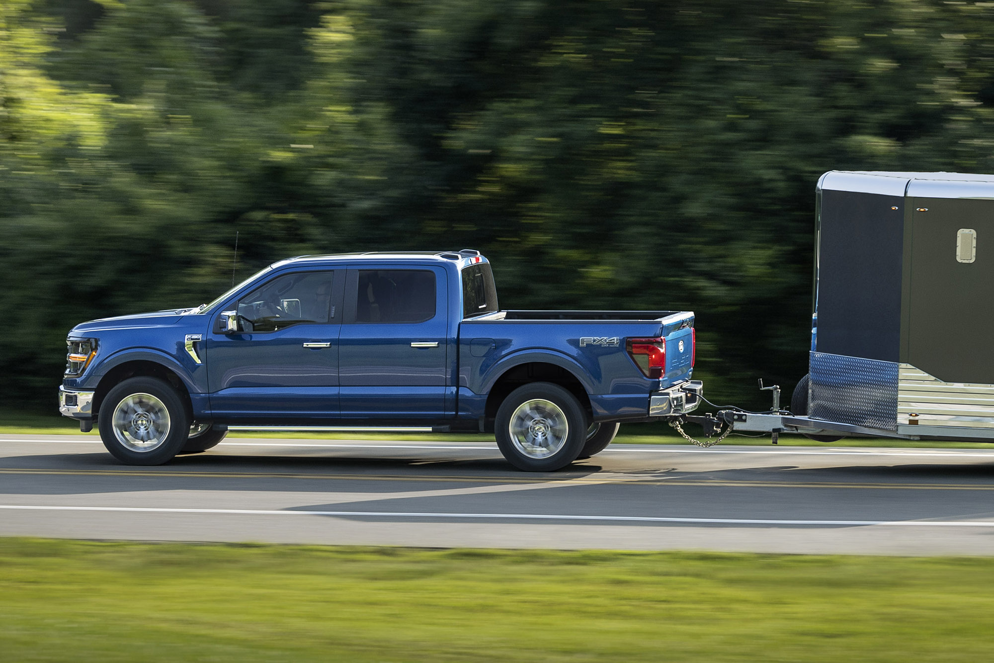 Ford F-150 in blue towing an enclosed trailer on a paved road.