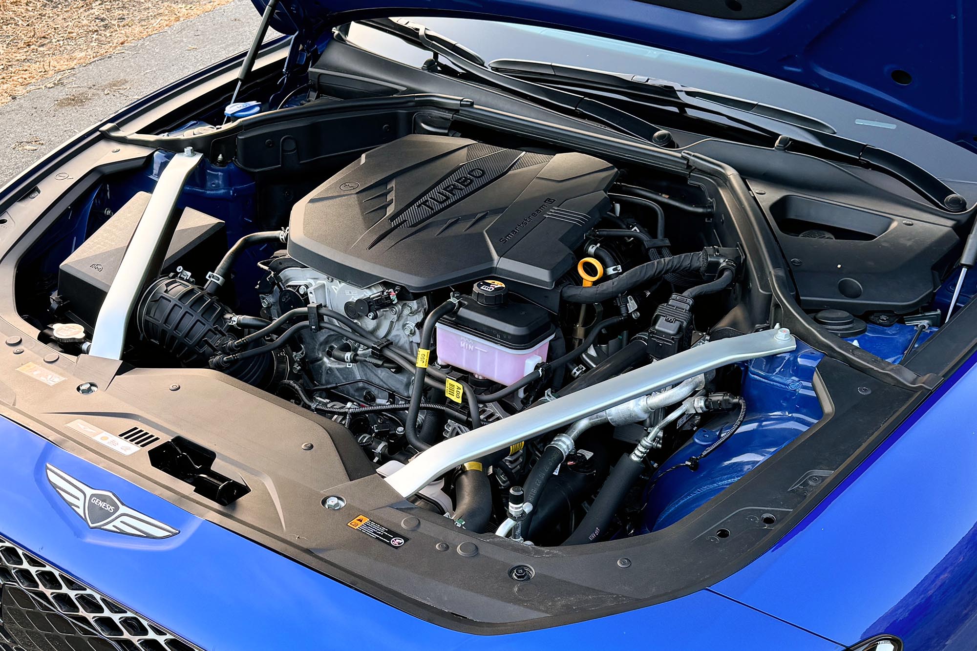 The engine bay of a blue 2024 Genesis G70 2.5T Sport Prestige showing the new turbocharged 2.5-liter four-cylinder