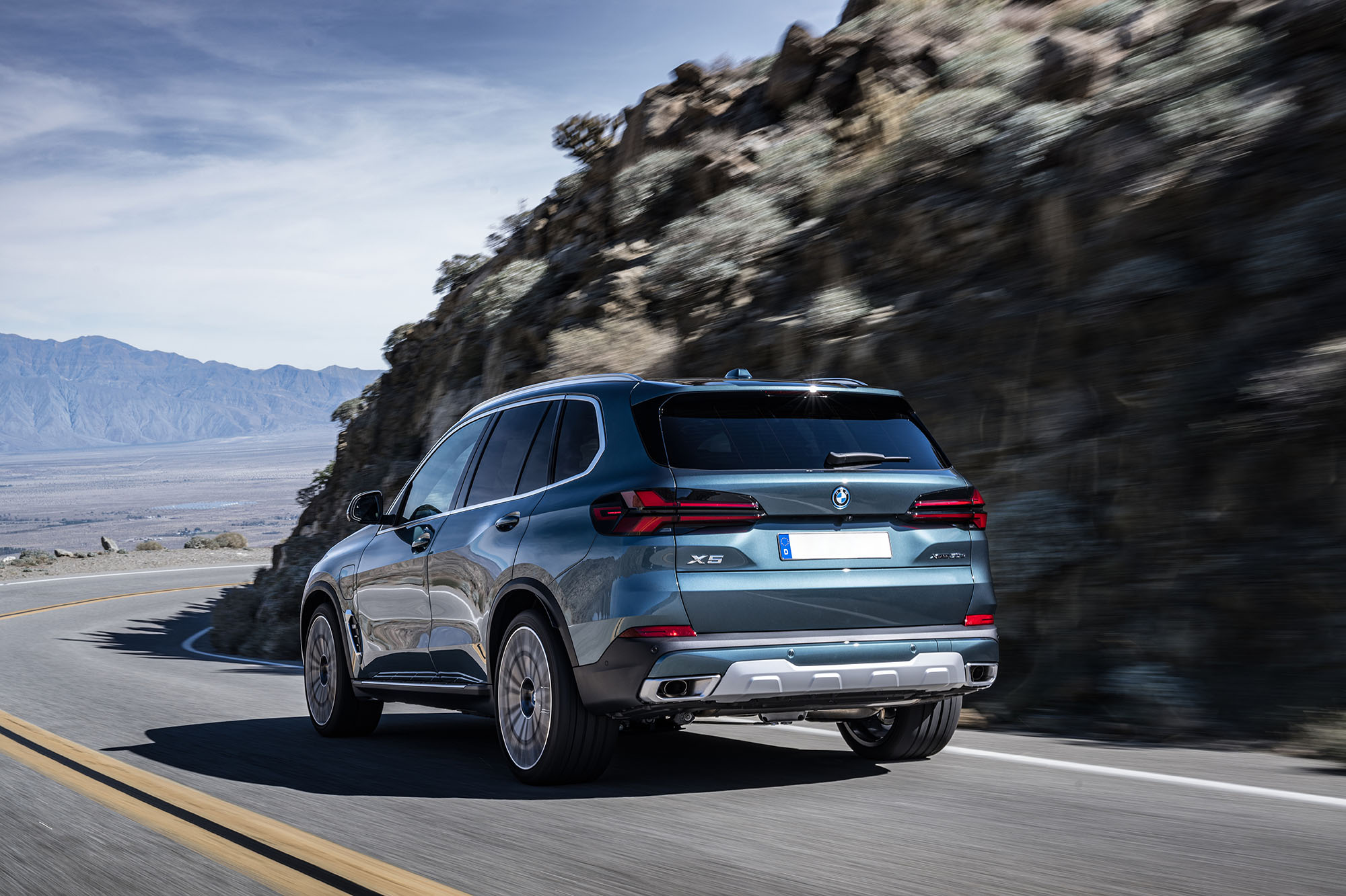 BMW X5 in green-blue driving on a paved road in the mountains.