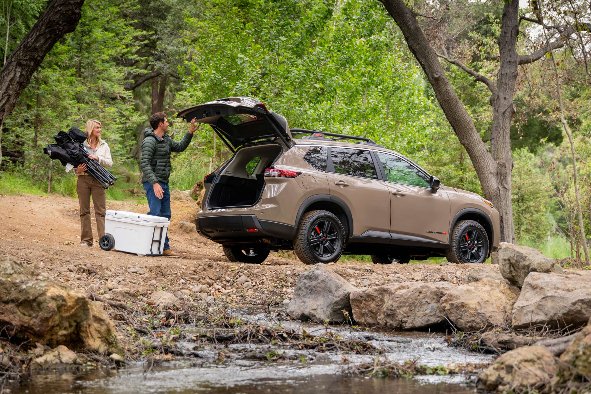 Side of a 2025 Nissan Rogue Rock Creek and two people placing gear in the back.