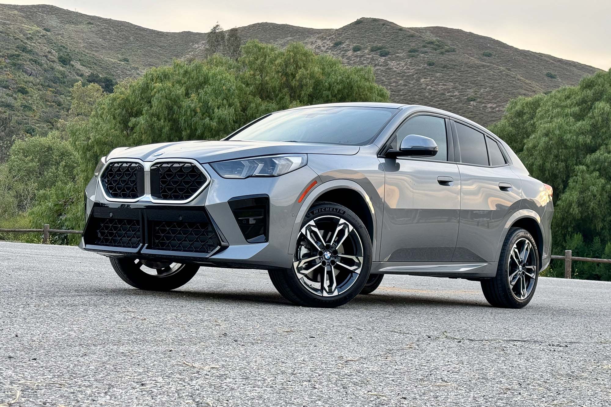 Gray 2024 BMW X2 parked on pavement with hills in the background.