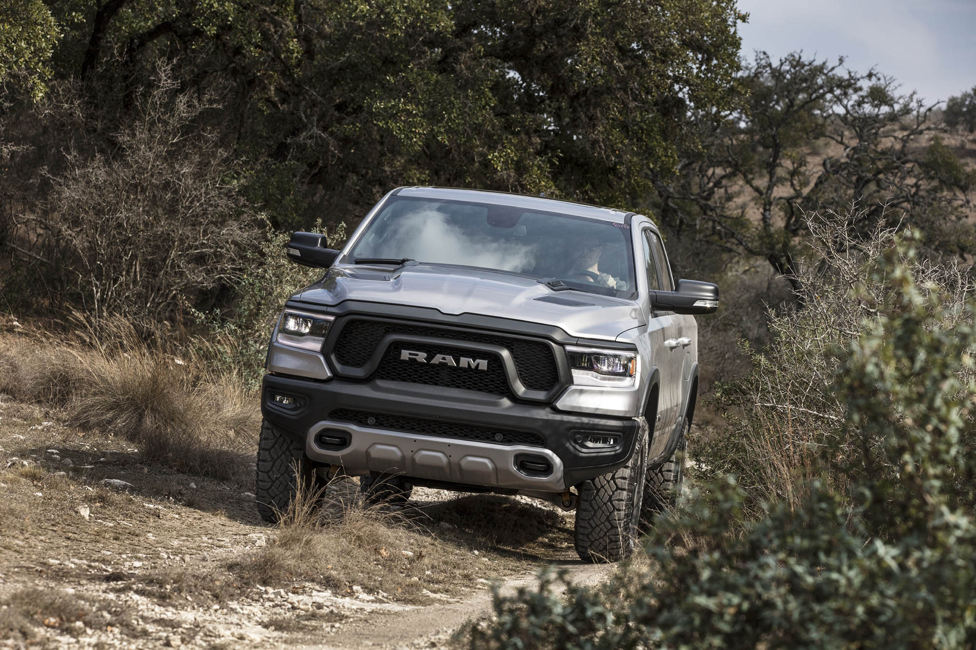 Silver Ram 1500 truck driving on dirt track.