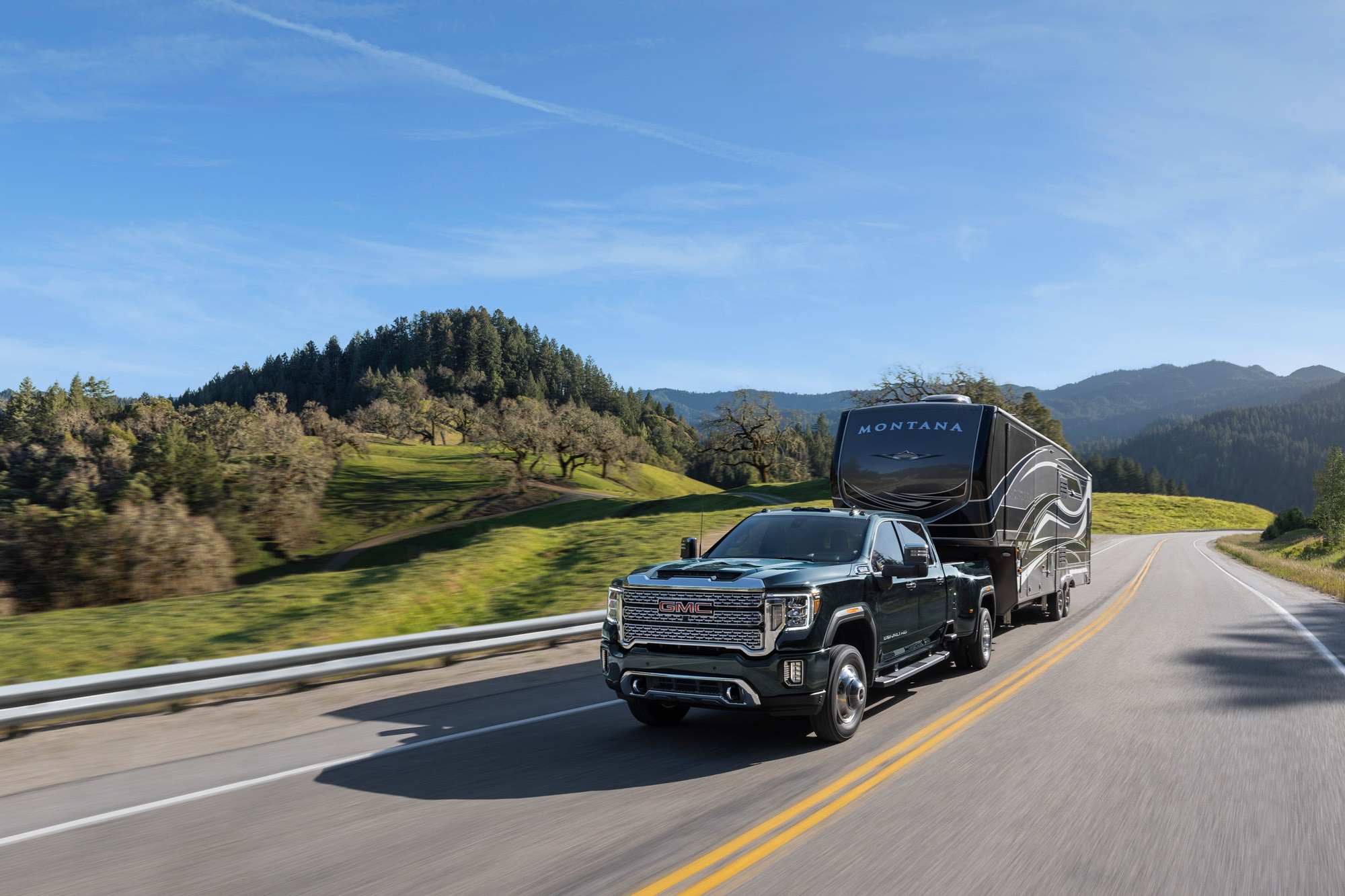 2023 GMC Sierra 3500HD towing travel trailer on rural highway.