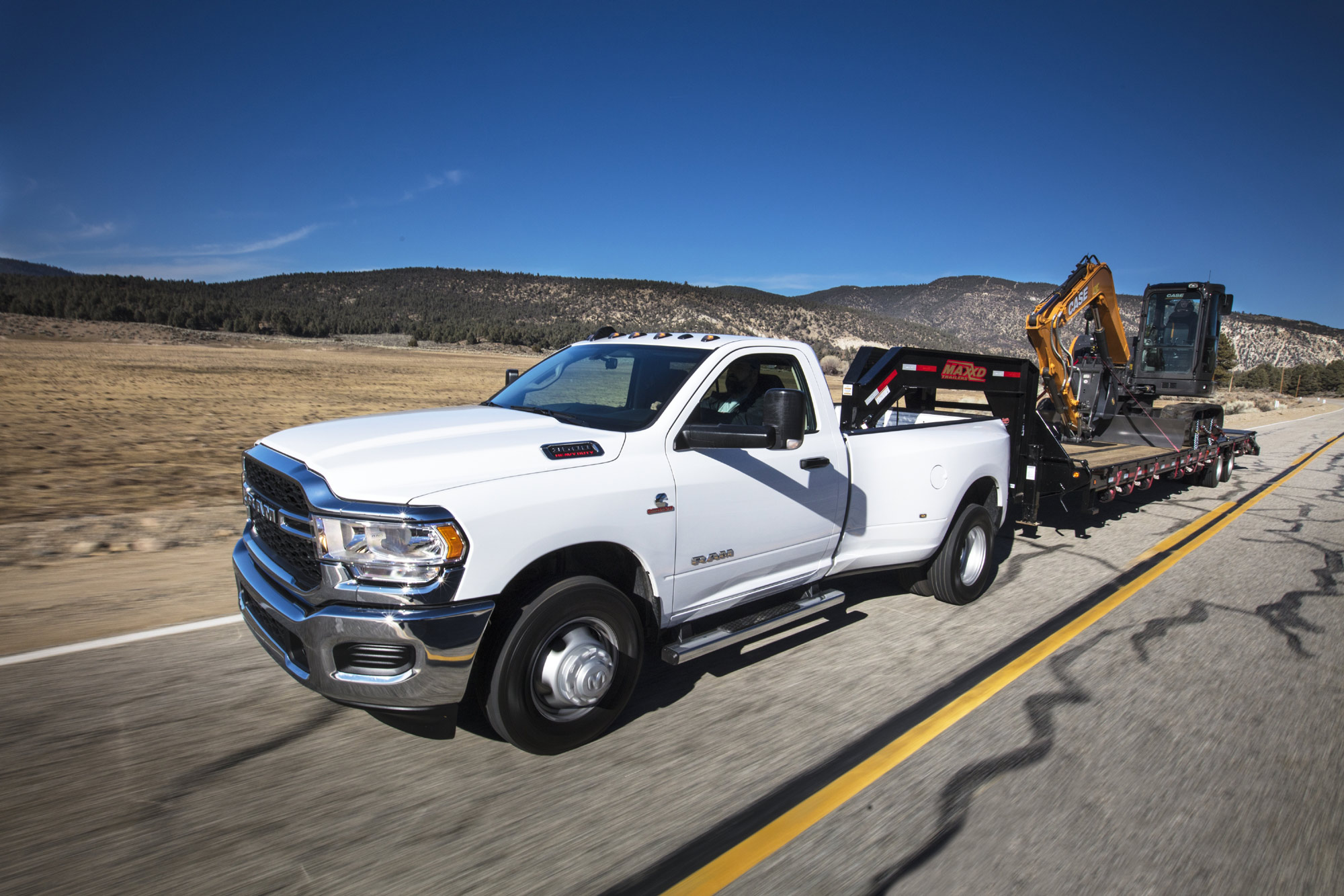 2024 Ram 3500 towing heavy equipment on a trailer down a highway.