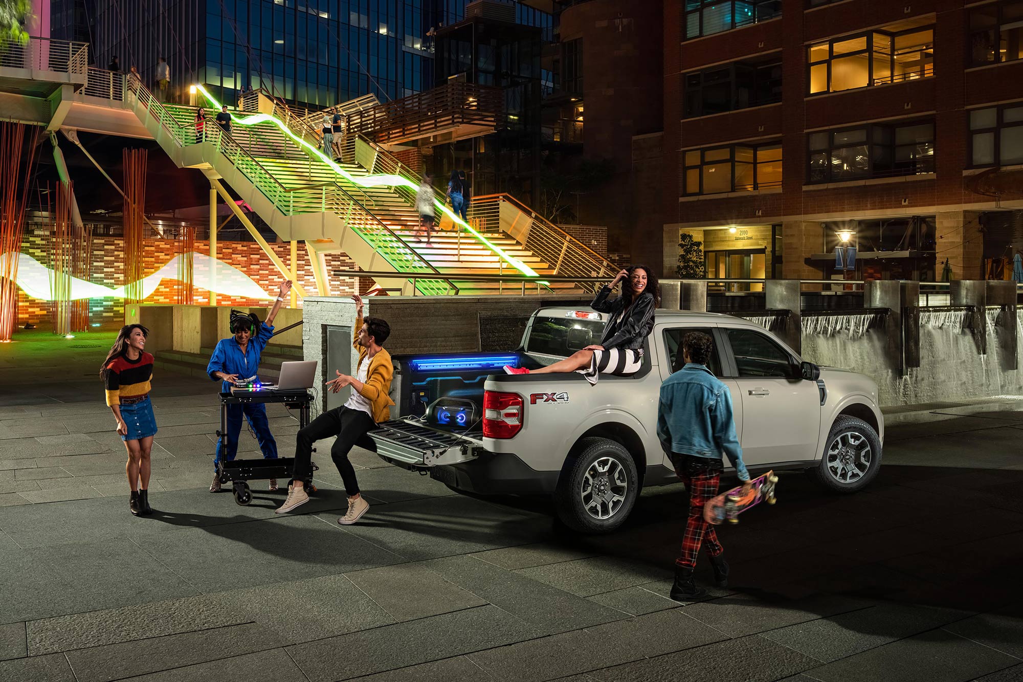 Several people tailgate around a silver Ford Maverick