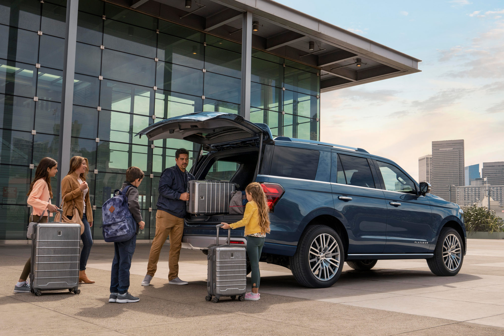 A family loads the back of a blue Ford Expedition