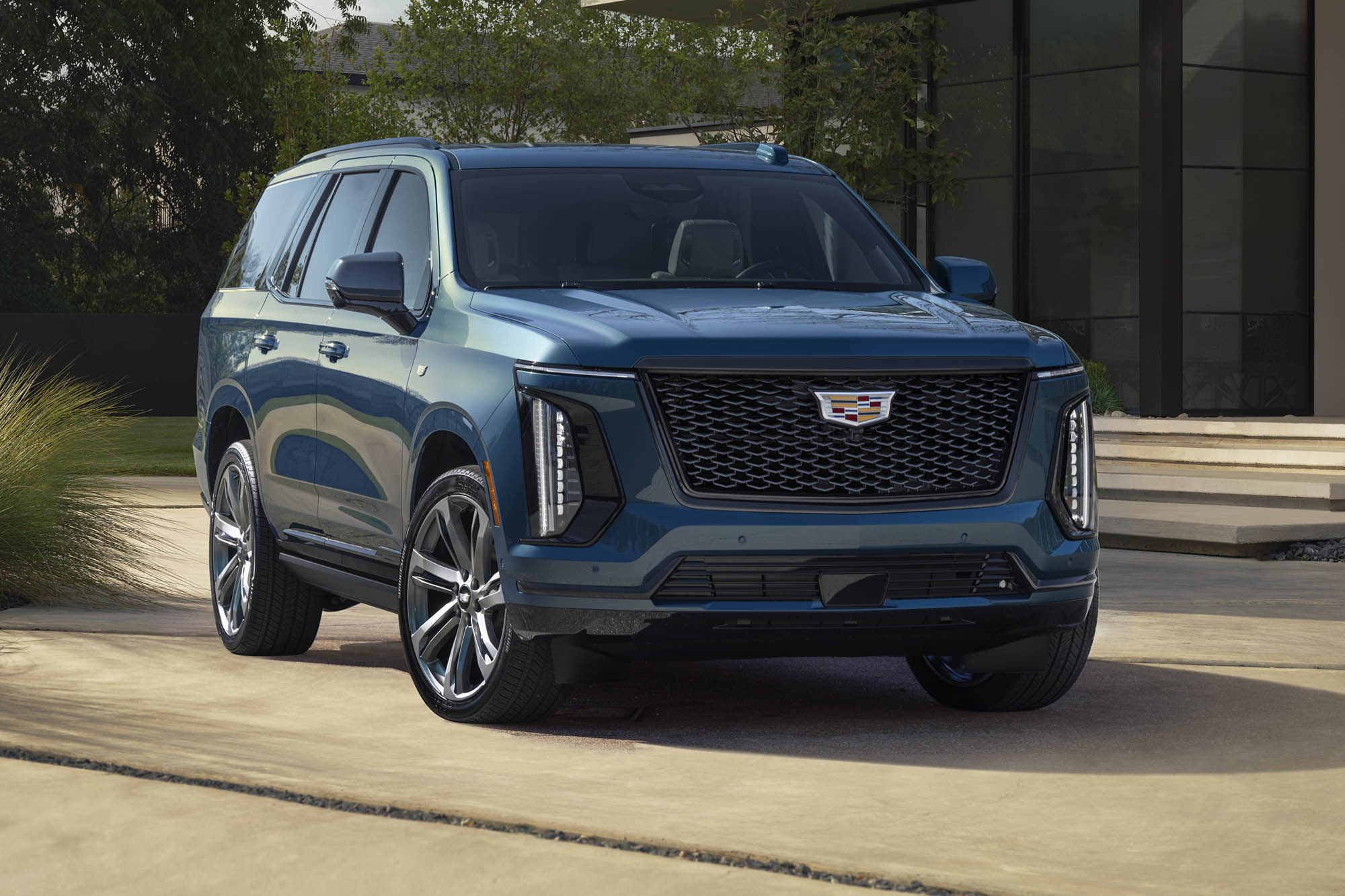 A front right view of a blue 2025 Cadillac Escalade parked in front of a modern home