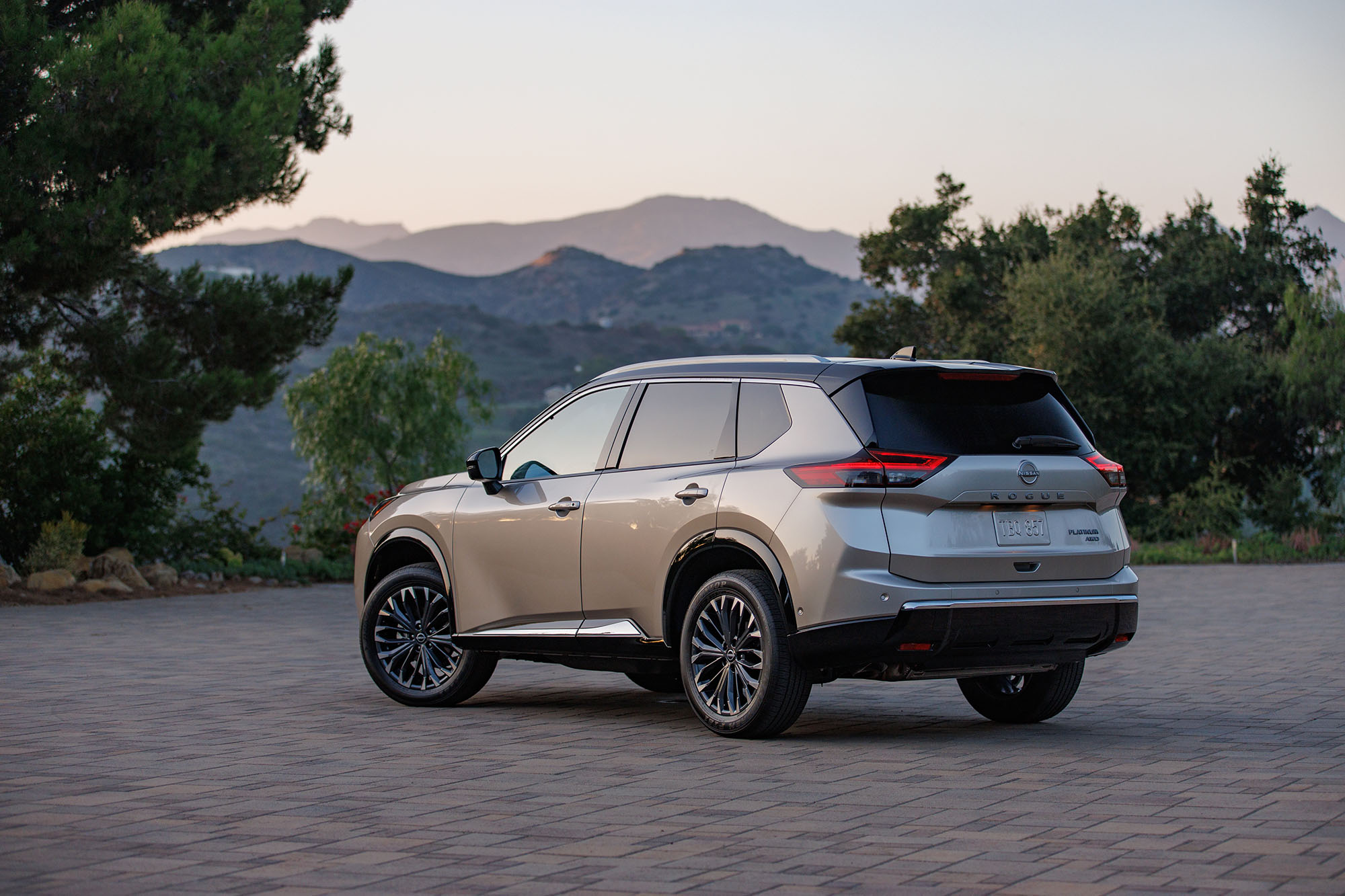 Tan Nissan Rogue parked on pavers overlooking mountains.