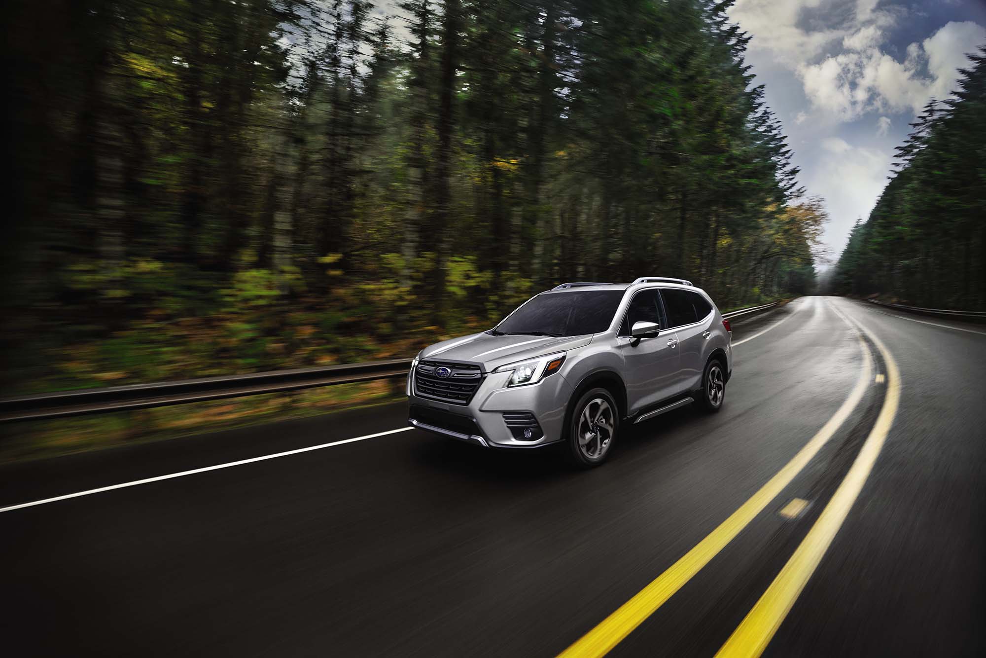 Gray Subaru Forester driving on a paved road through a wooded area.