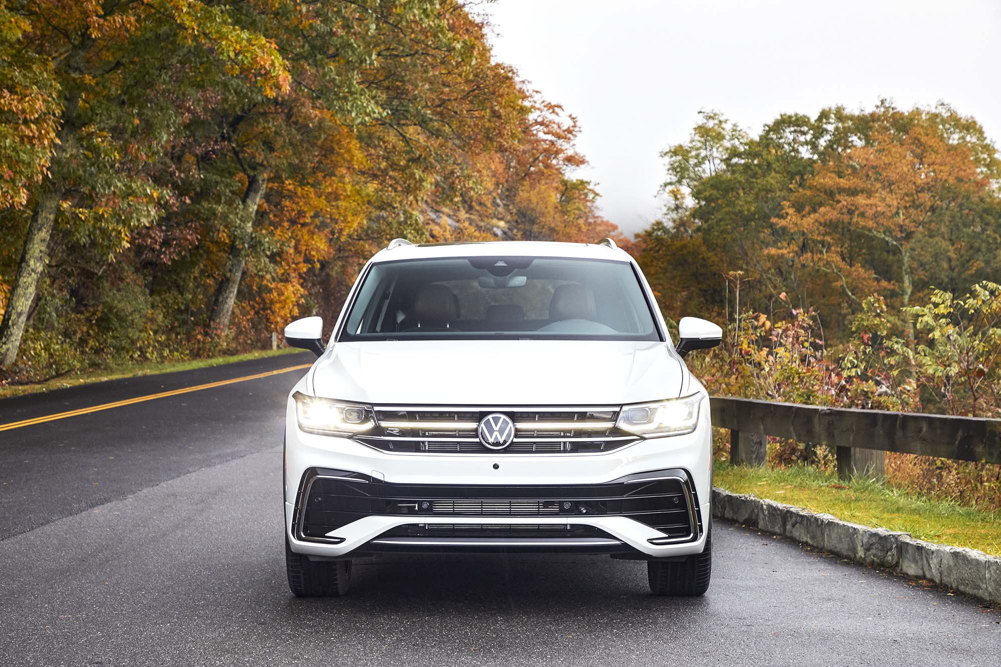 White Volkswagen Tiguan parked on a paved road with autumn foliage in the background.