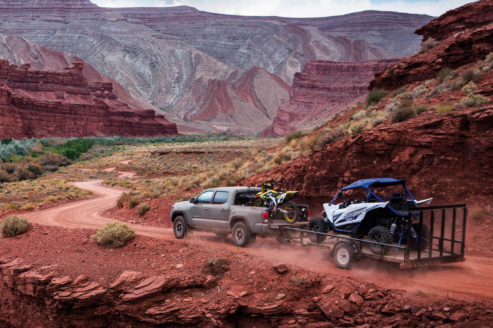 A Toyota Tacoma hauls a motorcycle and tows a trailer carrying an all-terrain vehicle