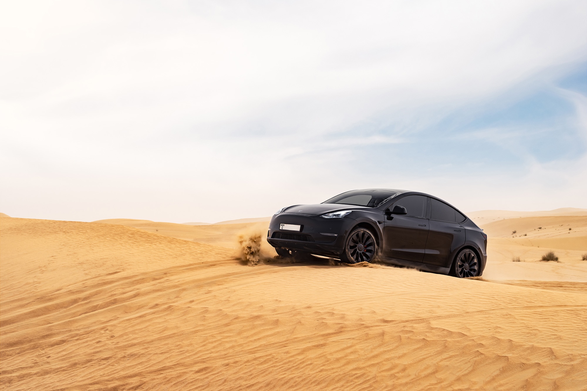 Black Tesla Model Y drives through deep sand.