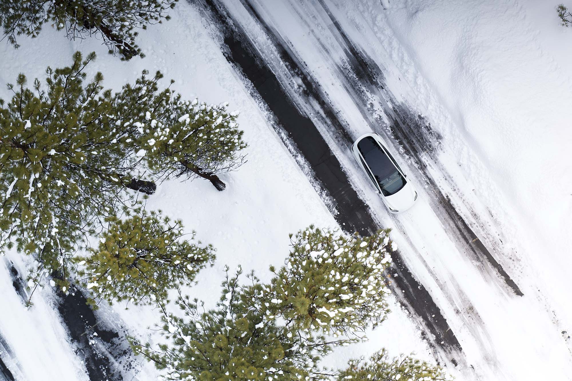 White Tesla Model Y drives on snowy road.