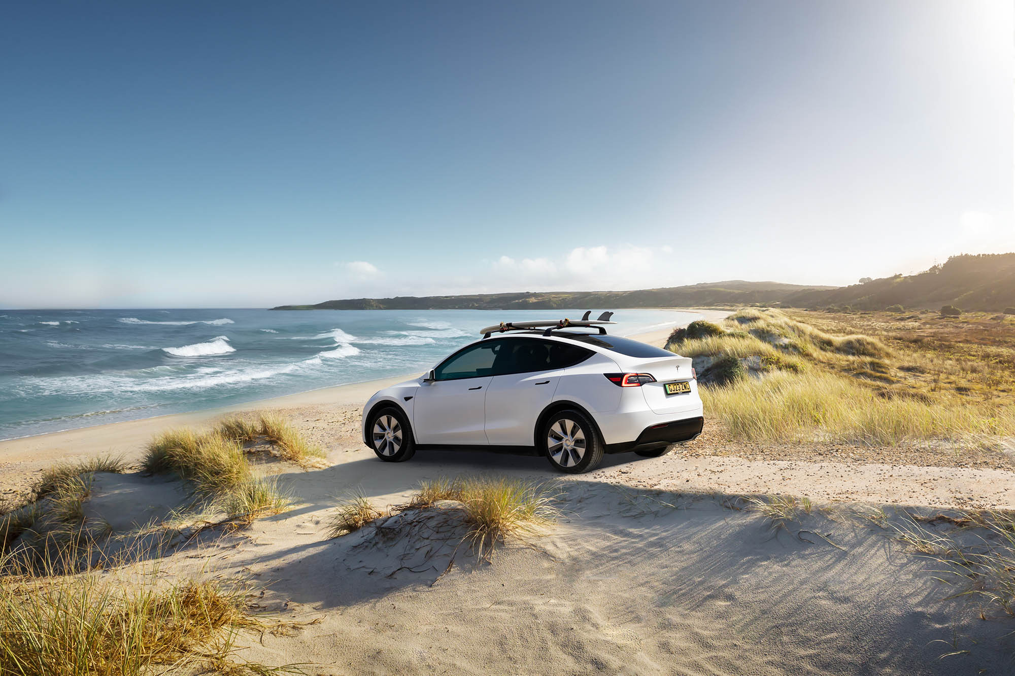 White Tesla Model Y drives onto a beach.