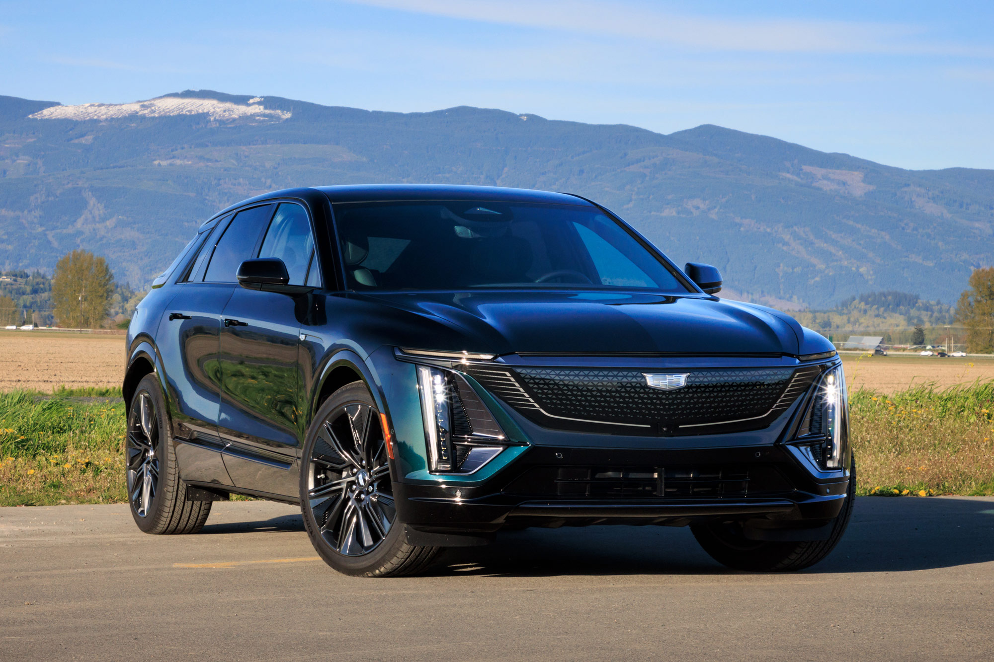 Front-quarter of a blue-green 2024 Cadillac Lyriq parked with mountains in the background